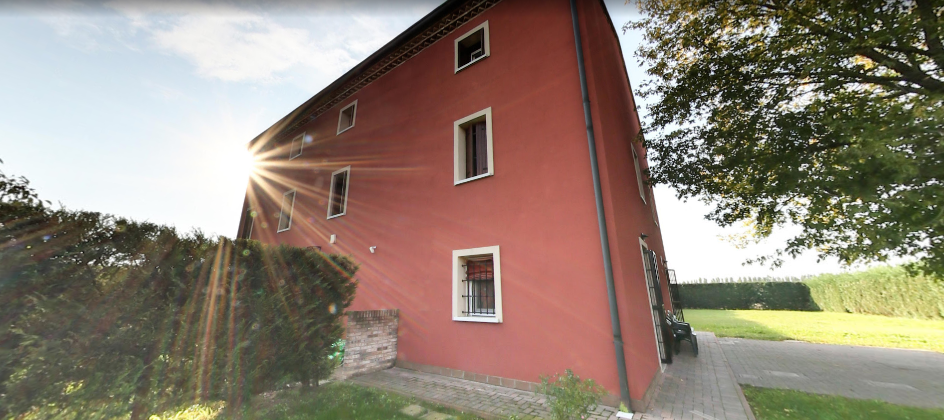 Un edificio rosso con numerose finestre che si staglia contro un cielo luminoso, con prato e alberi.