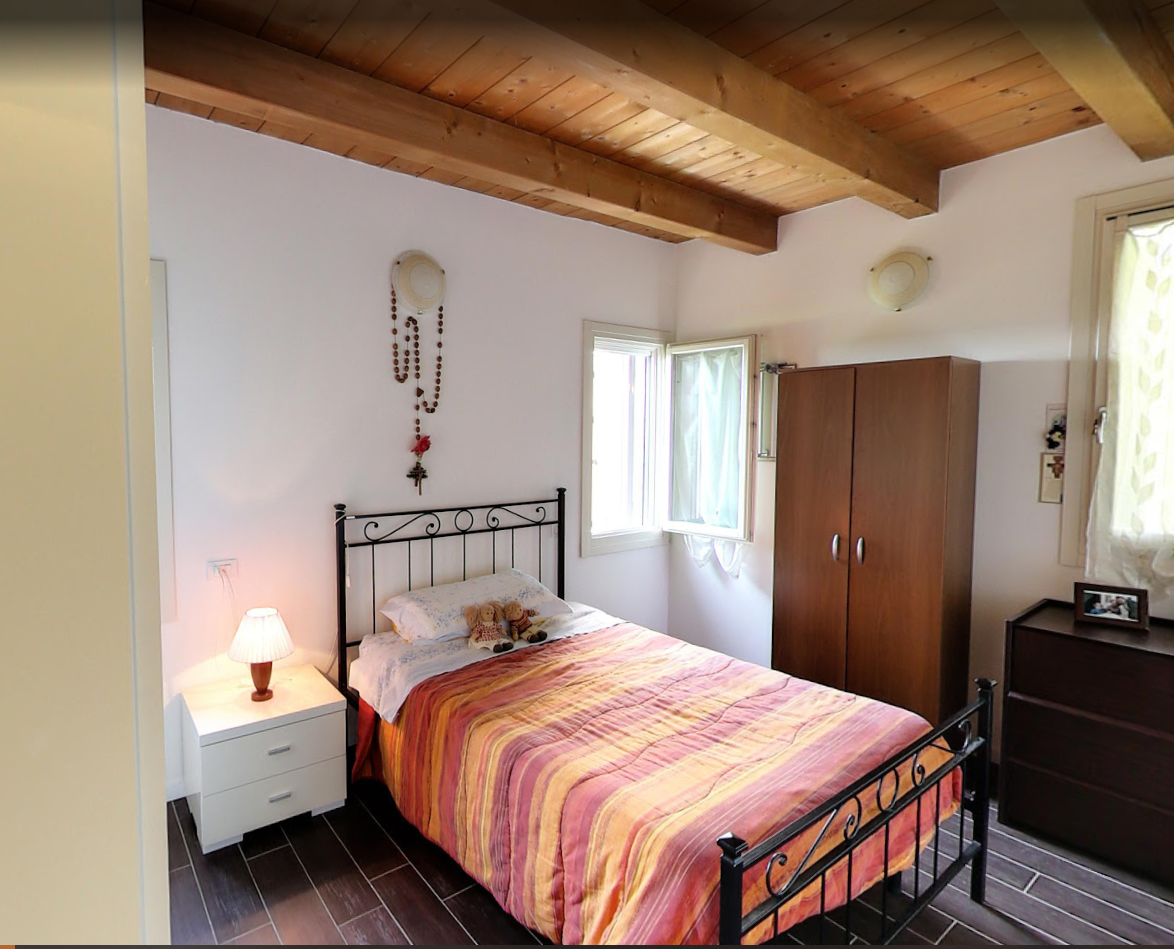 Camera da letto con letto singolo, comodino bianco, travi in ​​legno al soffitto e armadio.