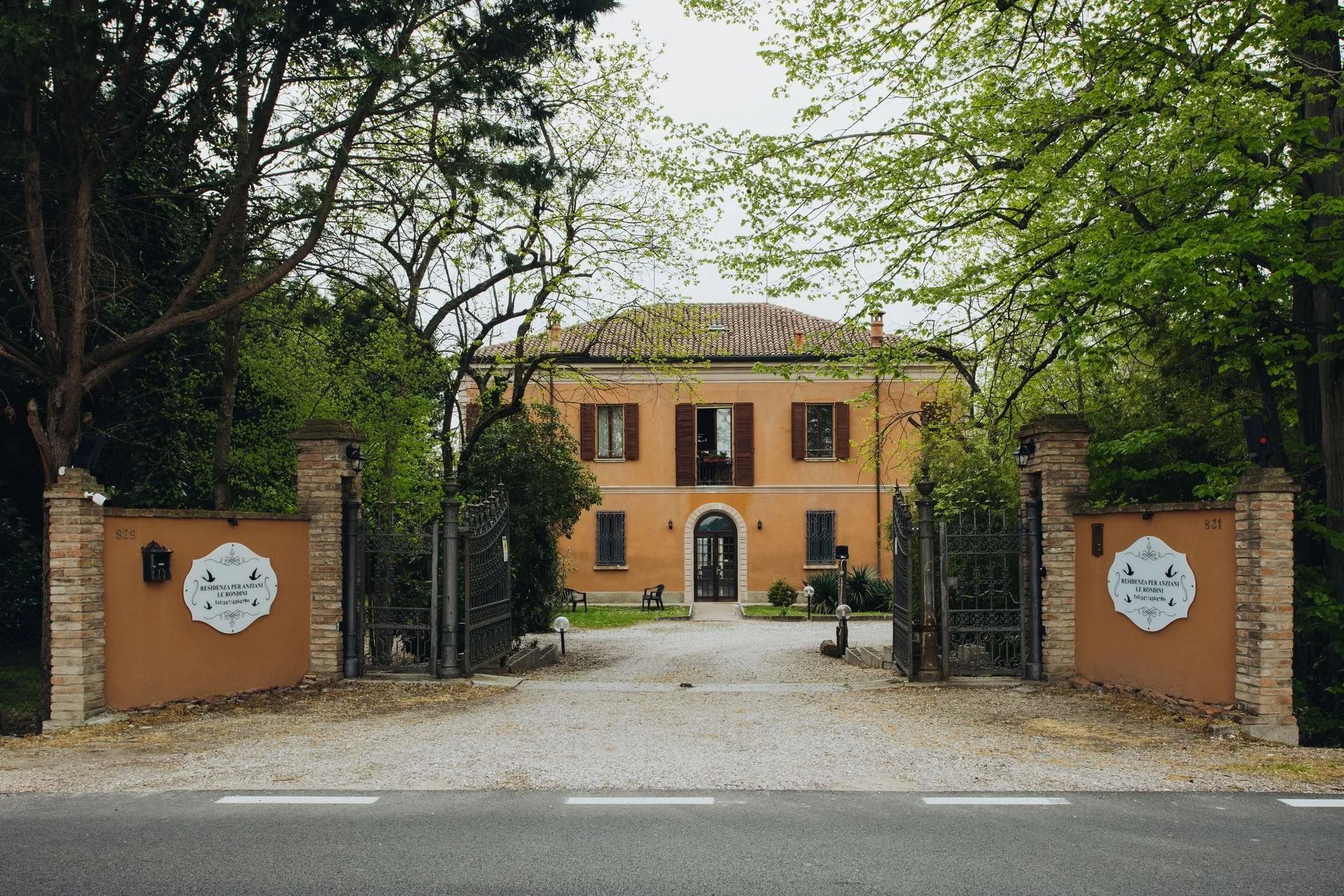 Casa in stucco arancione con ingresso recintato e lungo vialetto alberato.
