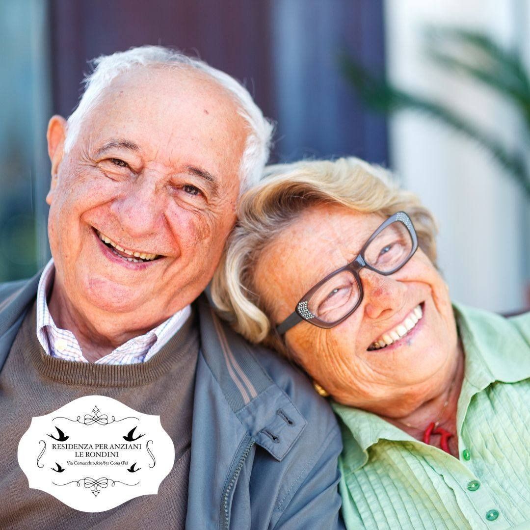 Coppia di anziani sorridenti, l'uomo con la giacca grigia, la donna con gli occhiali, con la testa appoggiata sulla spalla dell'uomo.