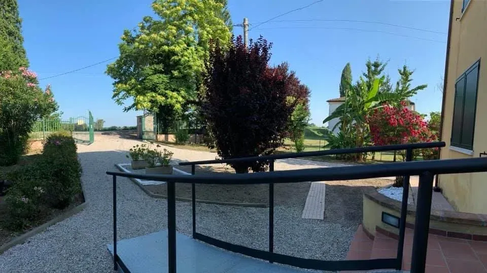 Rampa che conduce all'ingresso di un edificio. Sono visibili il sentiero di ghiaia, gli alberi e il cielo azzurro.