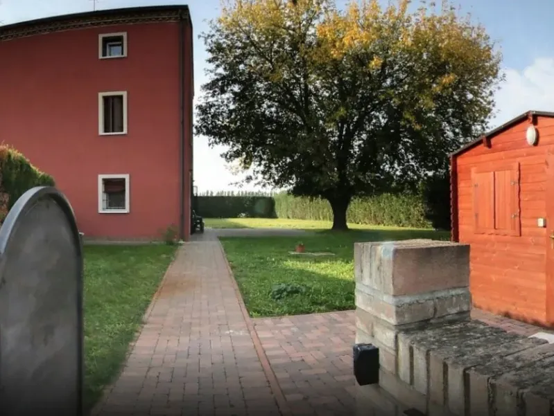 Edificio rosso e capannone con un sentiero in mattoni che conduce a un grande albero in un cortile erboso.