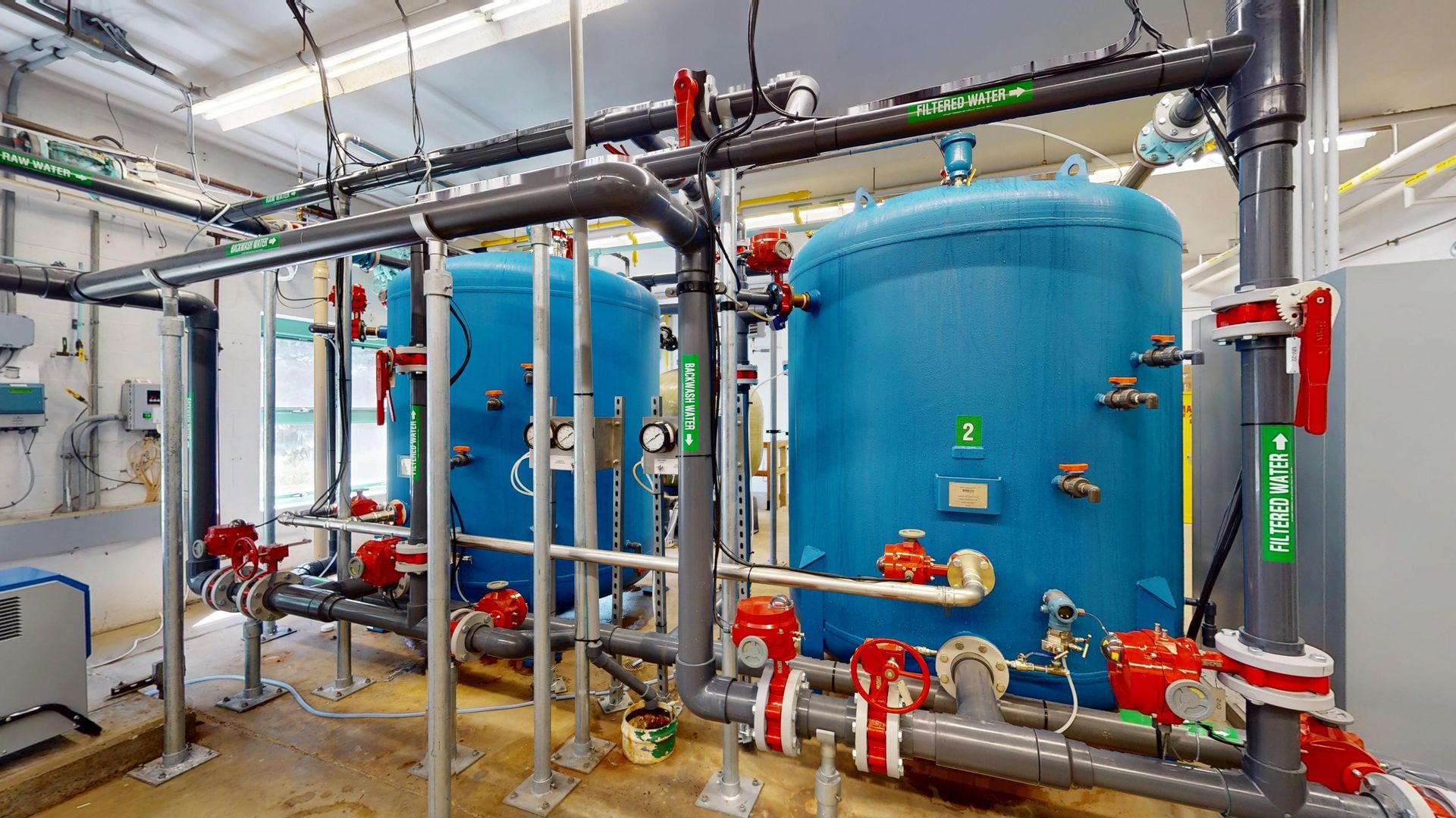 Blue industrial water filtration tanks with red valves and grey pipes in a water treatment facility