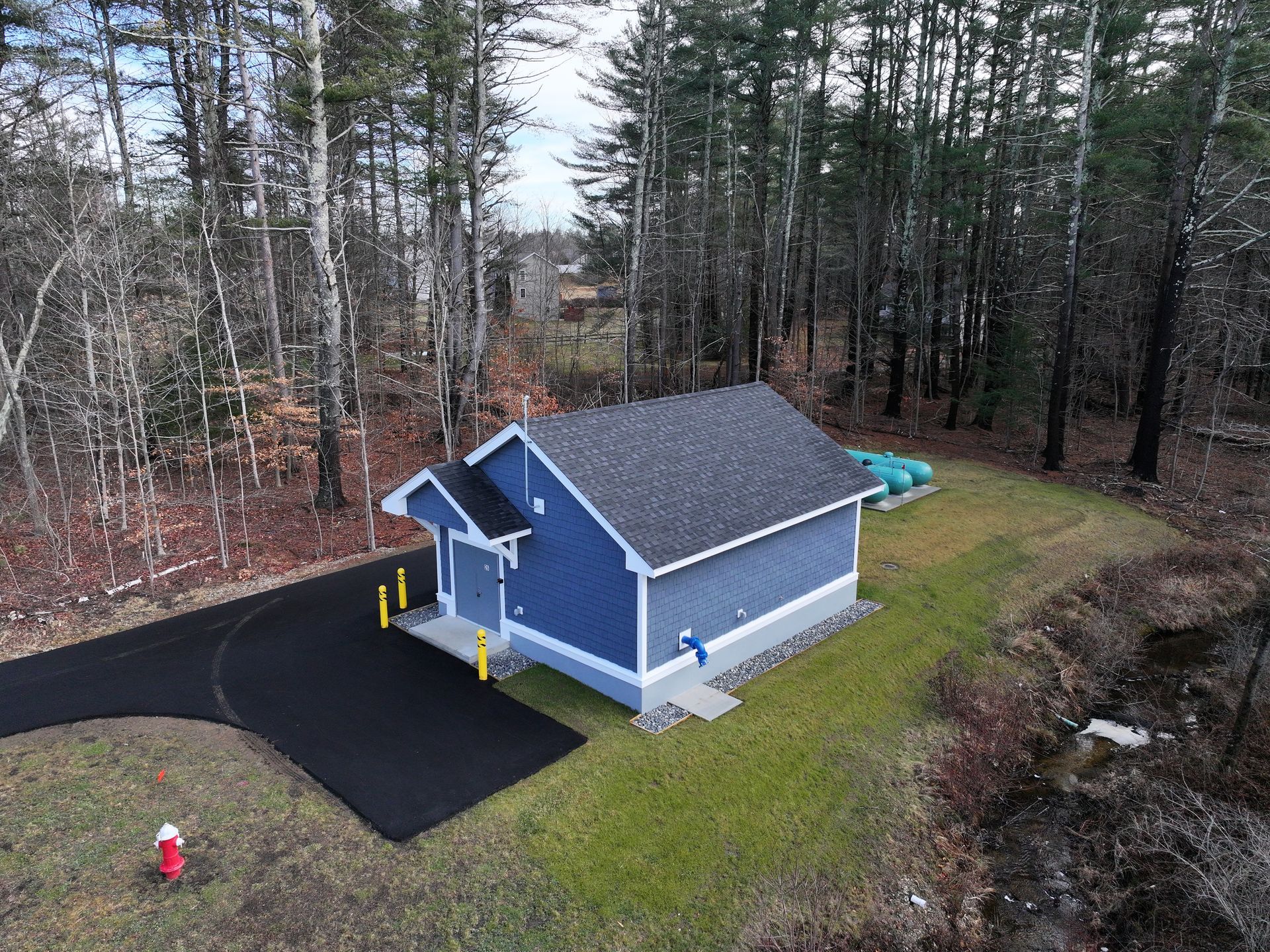 An aerial view of a small blue house in the middle of a forest.