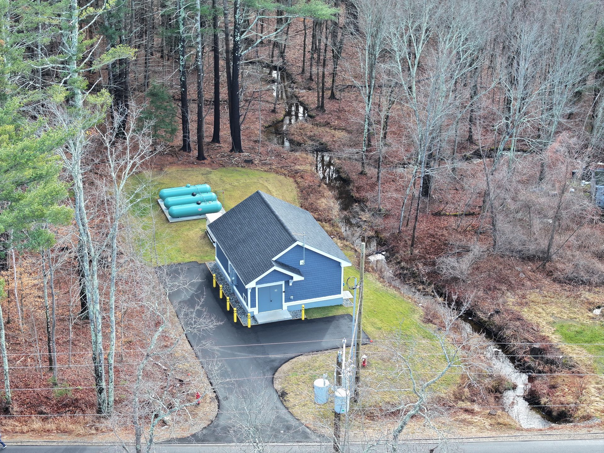 An aerial view of a small blue house in the middle of a forest.