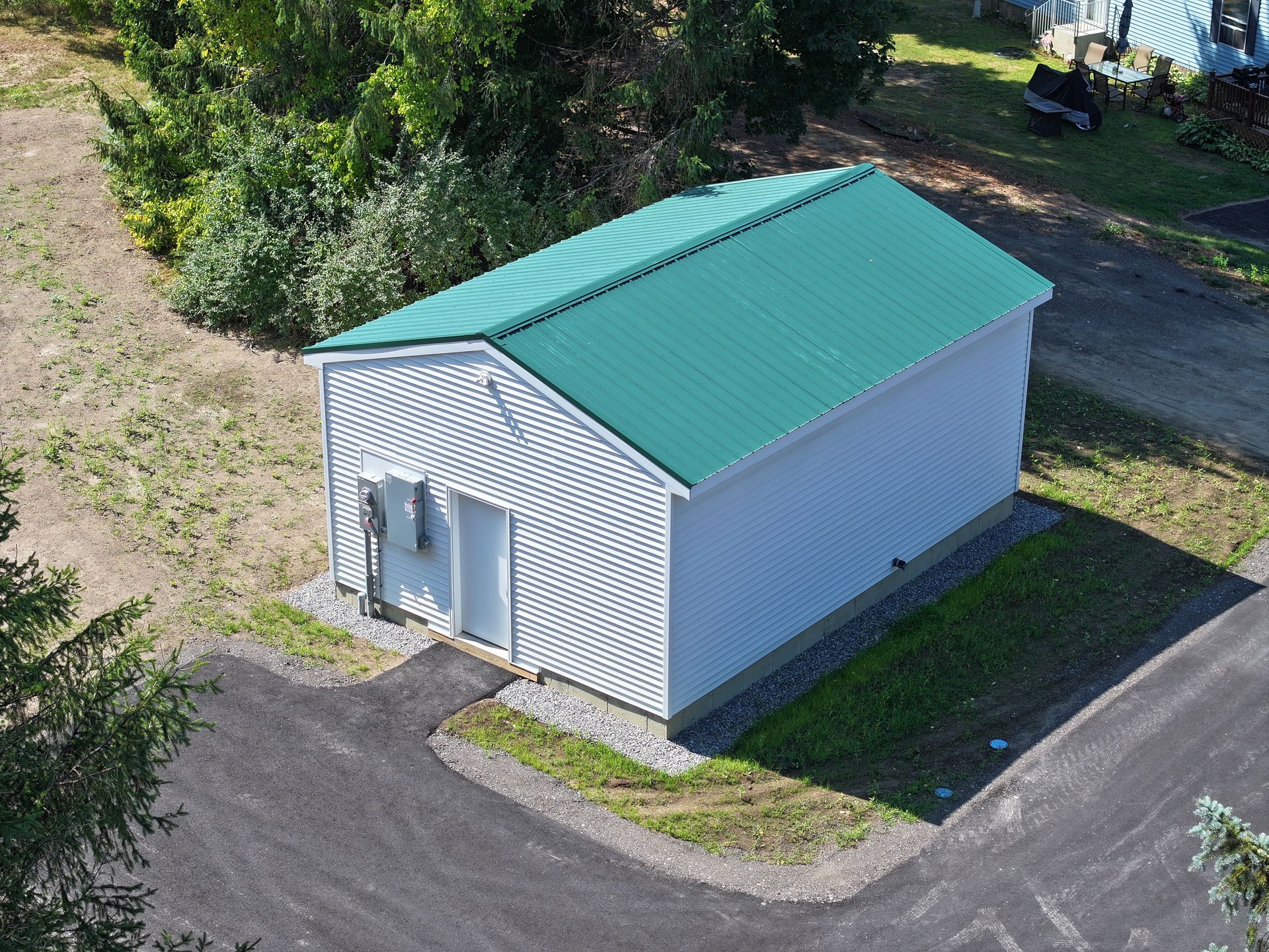 Small white utility building with a green roof, door, and AC unit.
