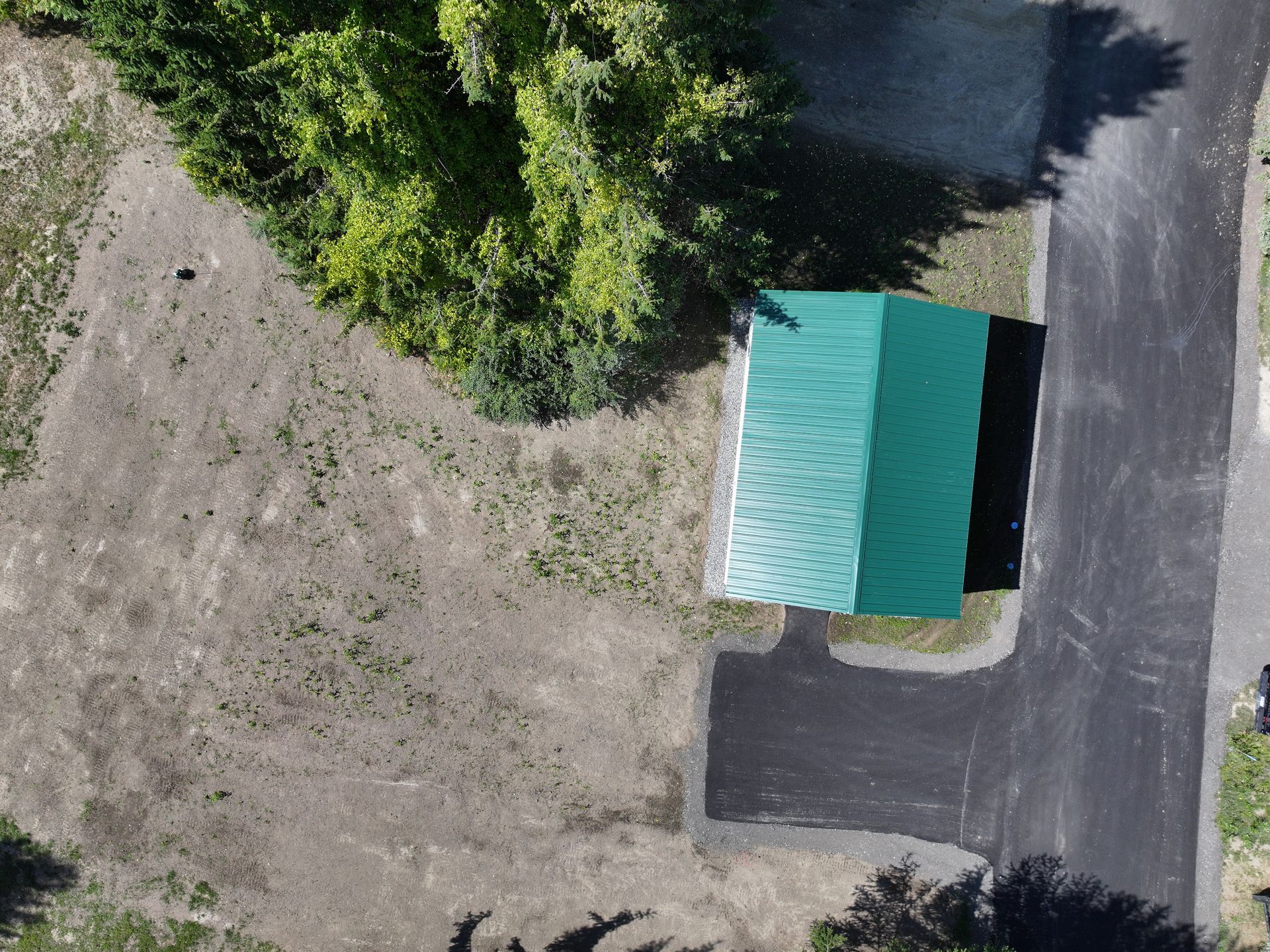 Overhead shot of a green-roofed building next to a paved road, next to a tree and field.
