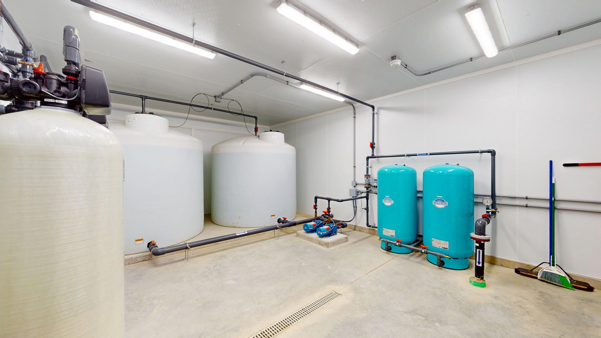 Water treatment room with white and turquoise tanks, pipes, and cleaning supplies.
