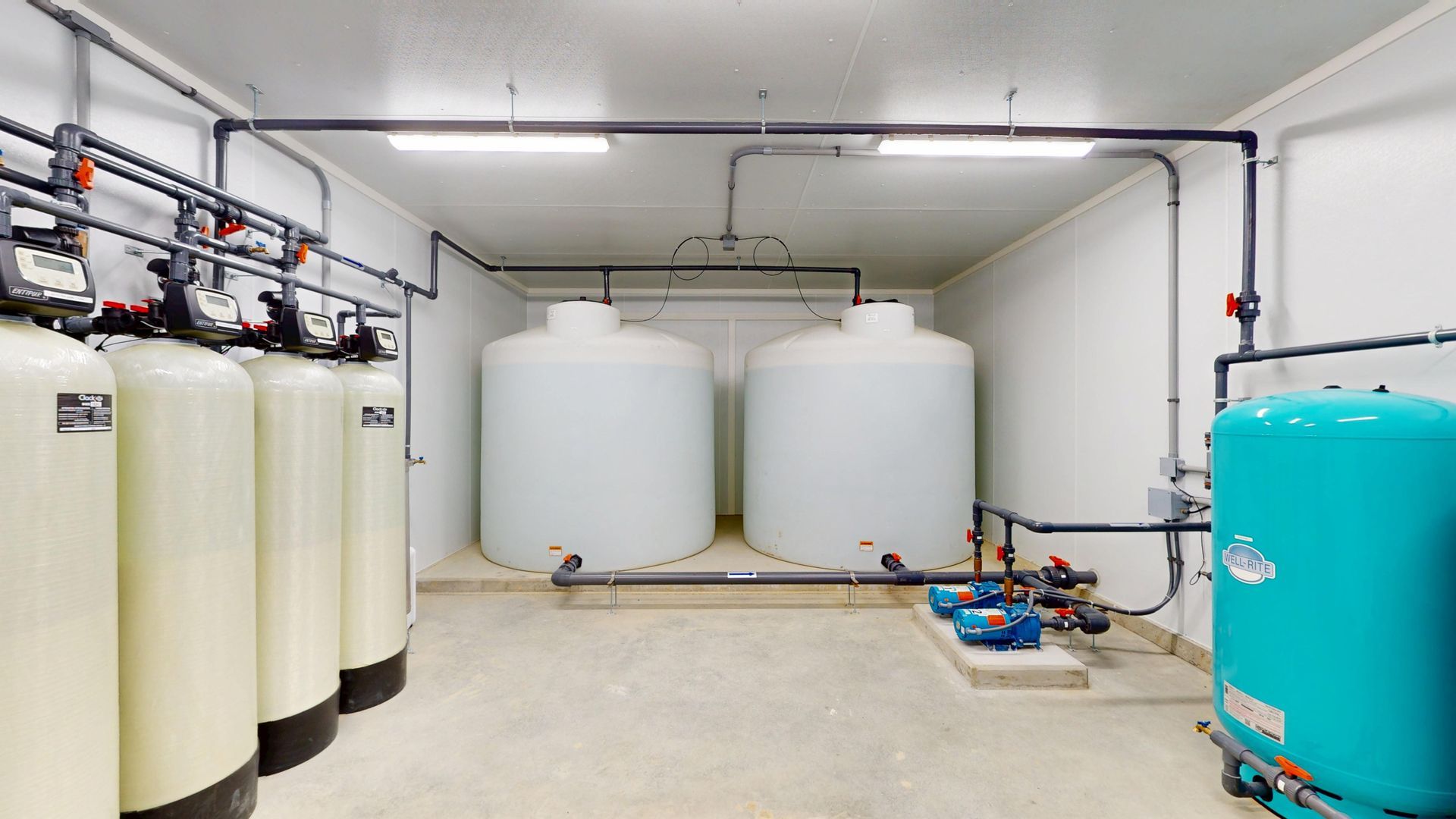 Water treatment room with tanks and pipes. Light beige columns, two white tanks, and a blue tank.