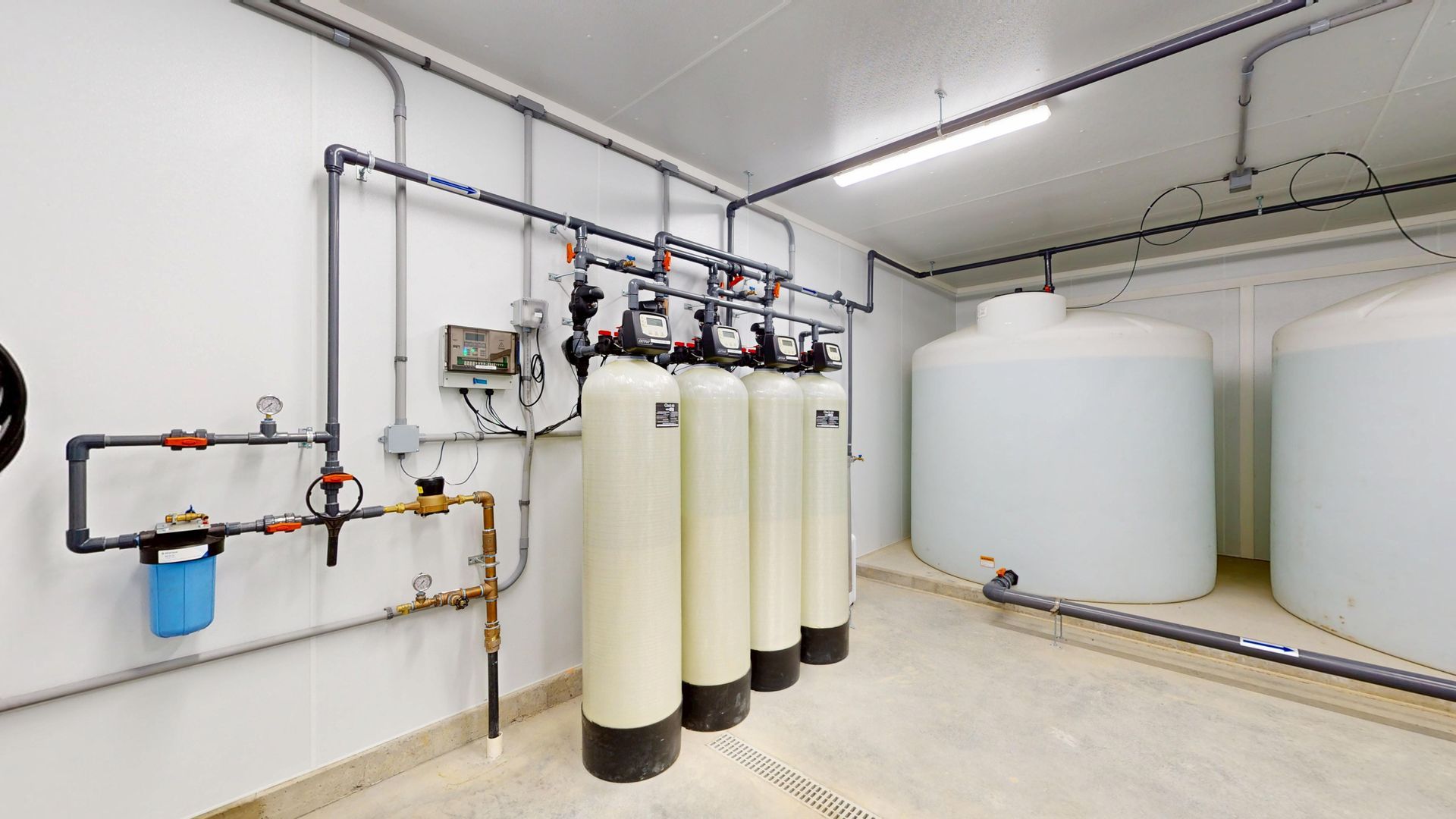 Water treatment system in a white room with tanks, pipes, and filters.