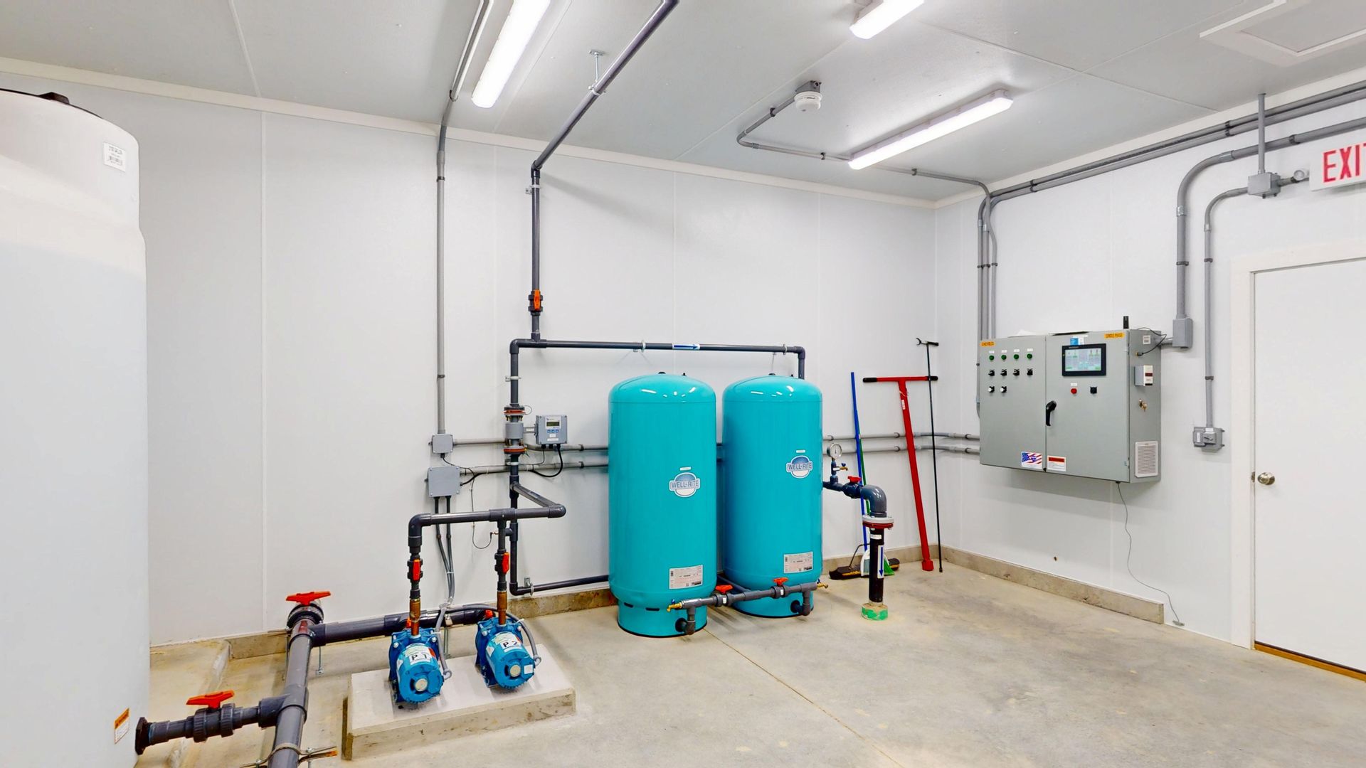 Water treatment equipment room with blue tanks, pipes, and control panel.