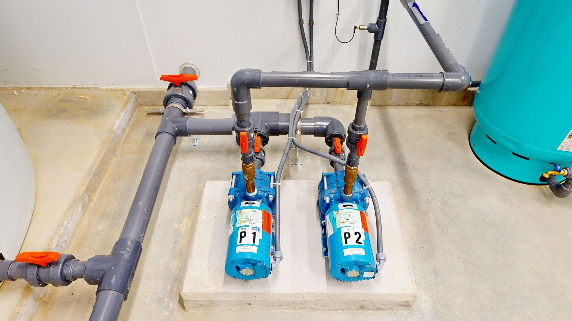 Two blue pumps labeled P1 and P2 with gray pipes and orange valves, in a utility room.