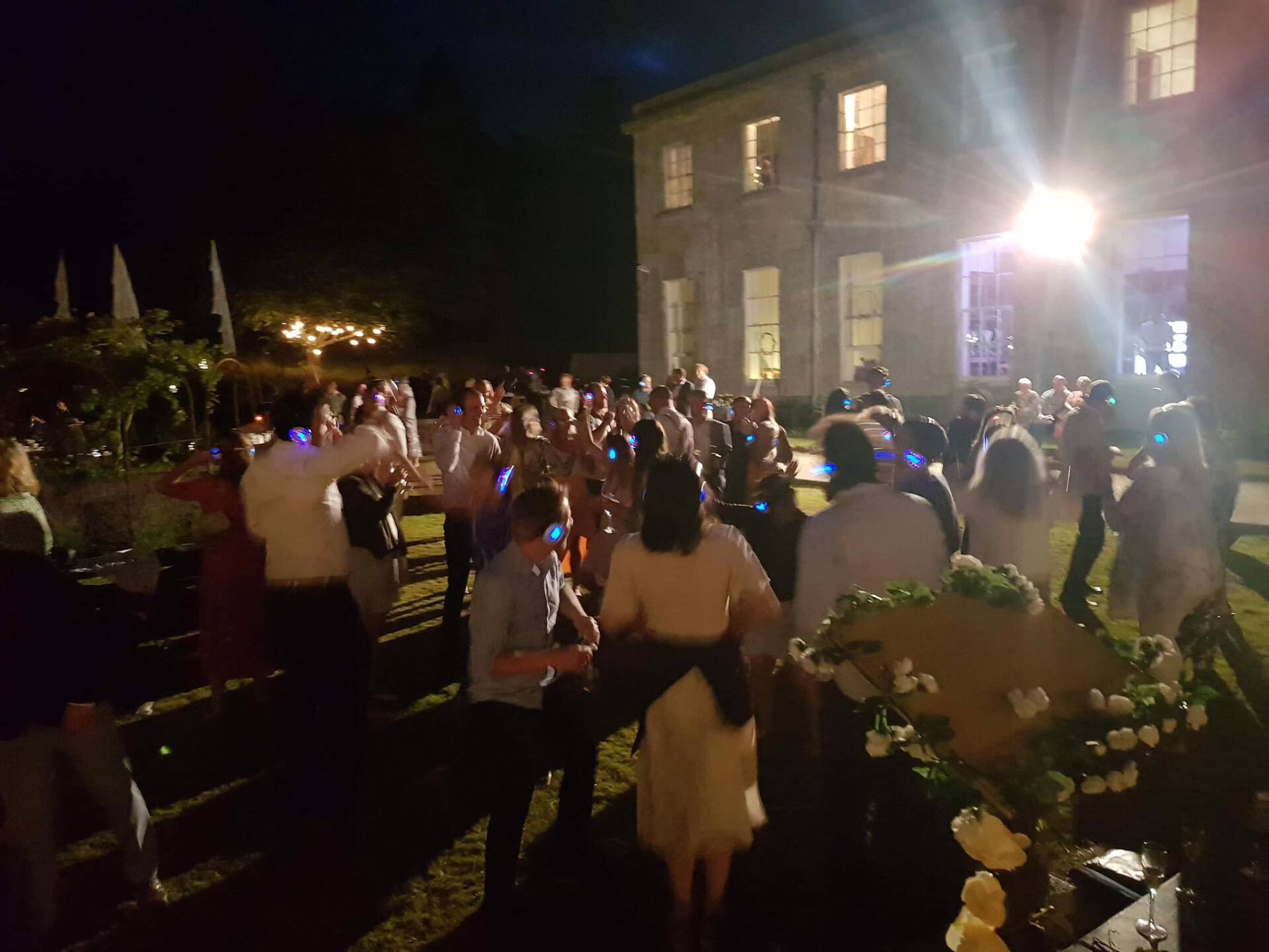 People dancing outdoors at night, illuminated by lights and a large building in the background.