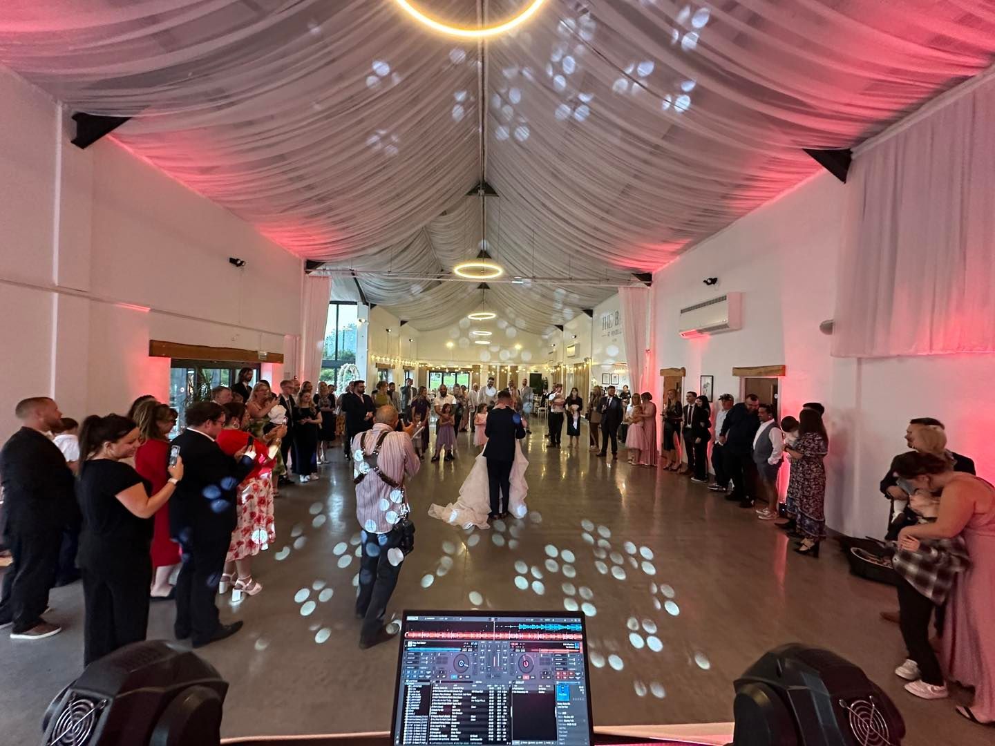 Bride and groom dance at wedding; guests watch. Star lights illuminate. Stone wall, staircase visible.