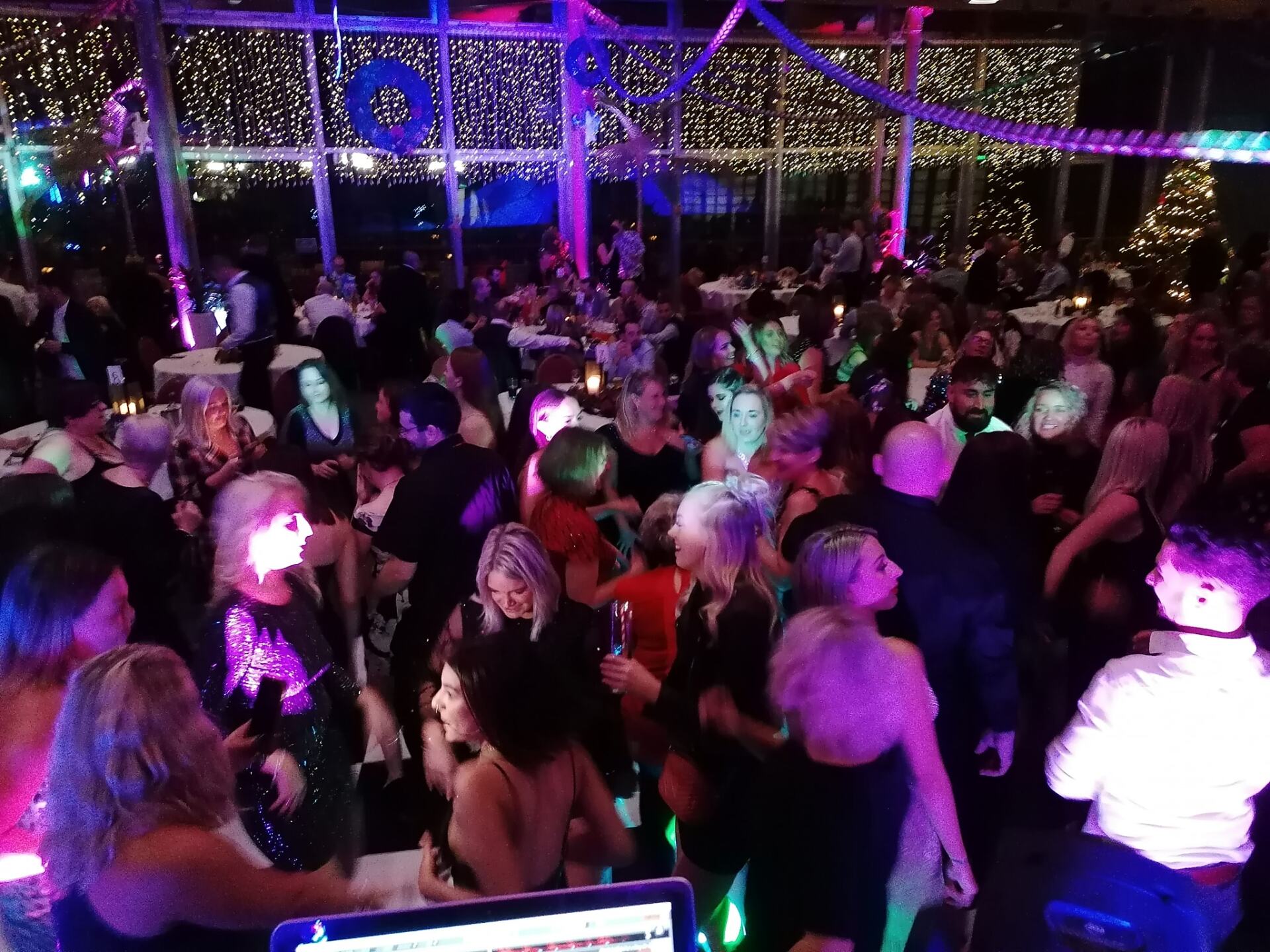 Partygoers dancing and mingling in a brightly lit event space with DJ equipment in the foreground.
