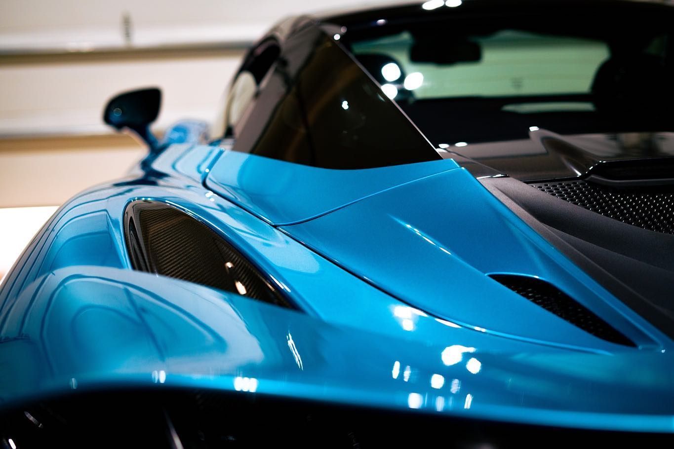 Close-up of a bright blue sports car hood and windshield in a showroom