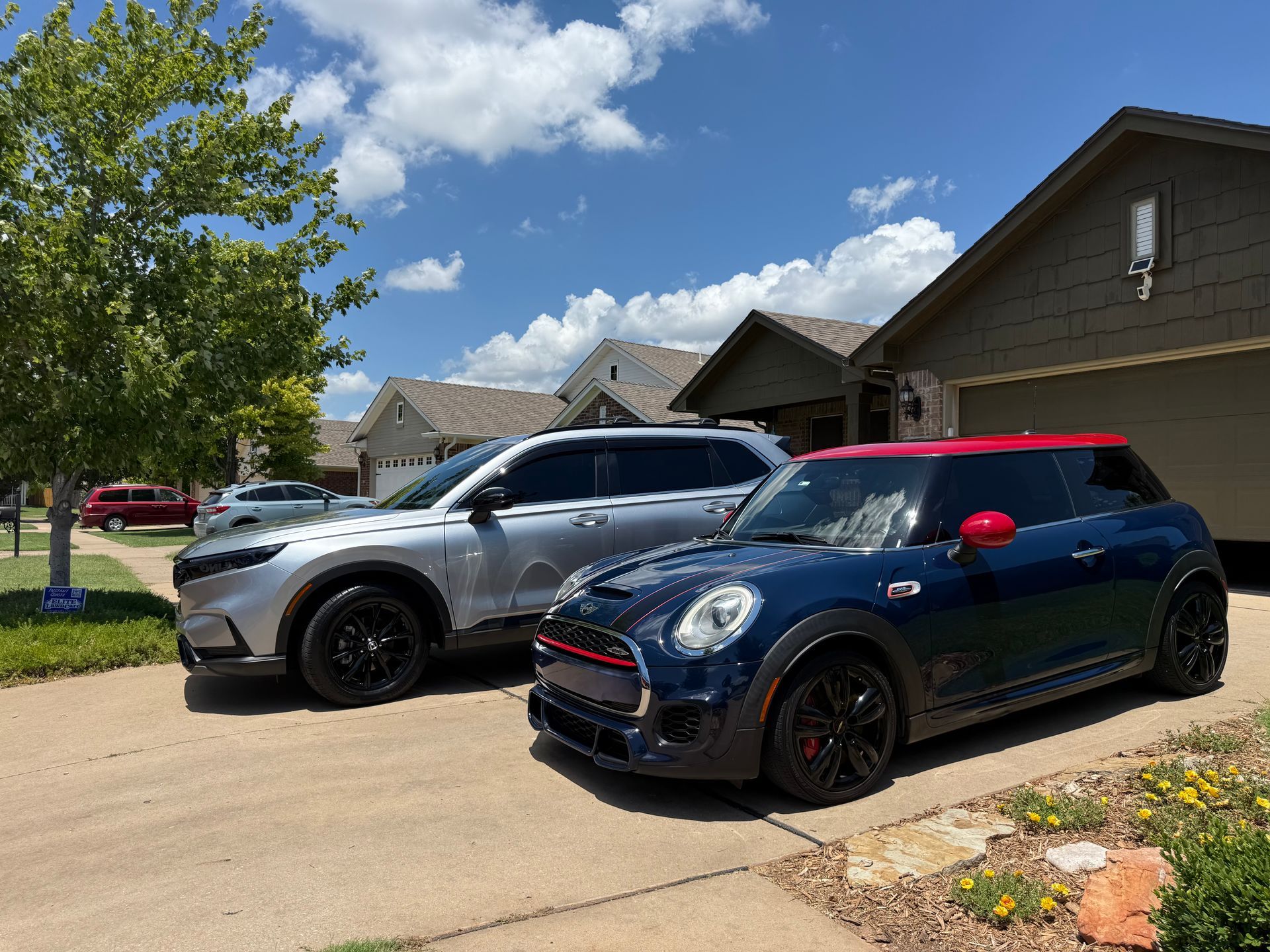 Two parked SUVs, a blue Mini and a silver crossover, in a suburban driveway under a sunny sky