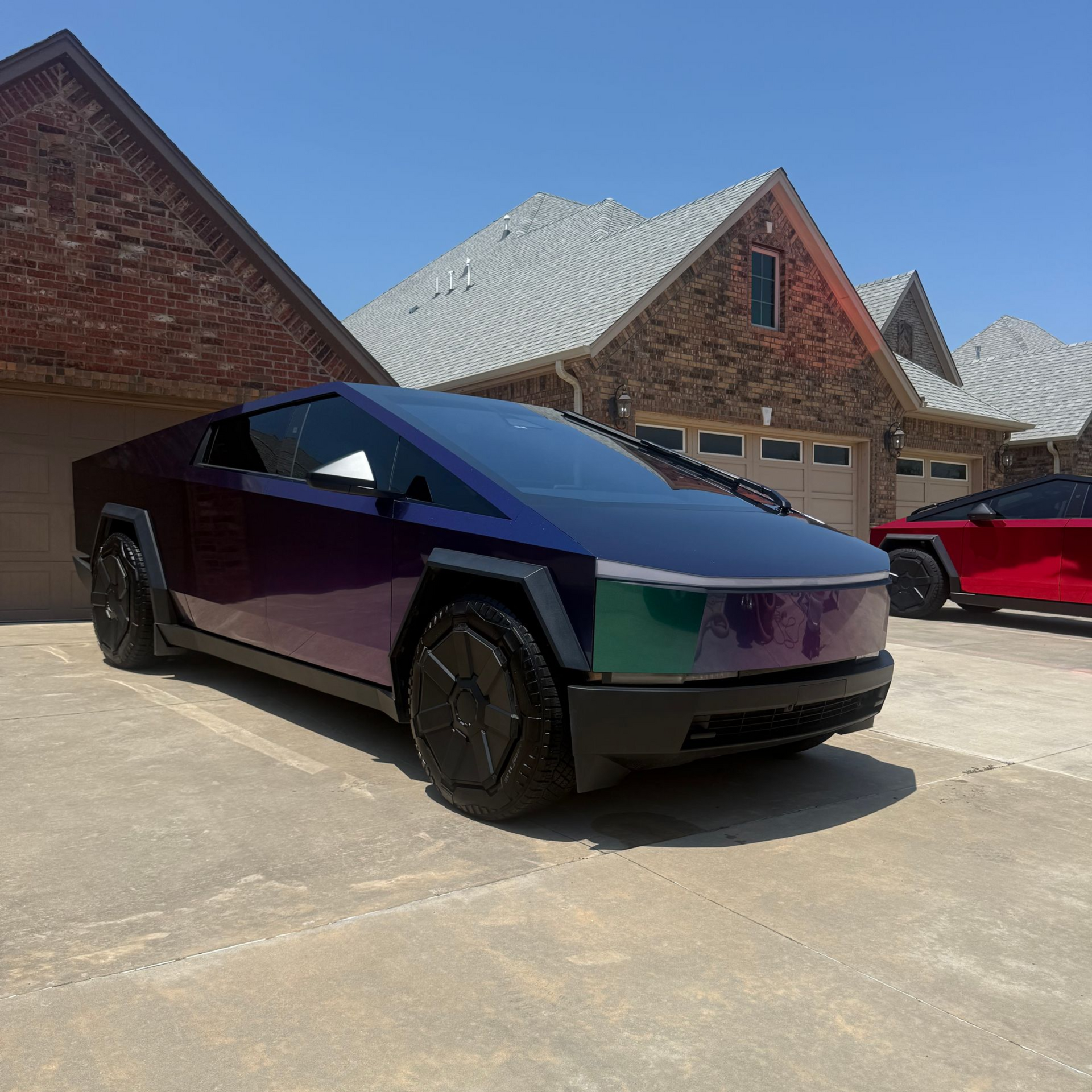Purple-black futuristic pickup parked in a driveway beside brick houses under a blue sky