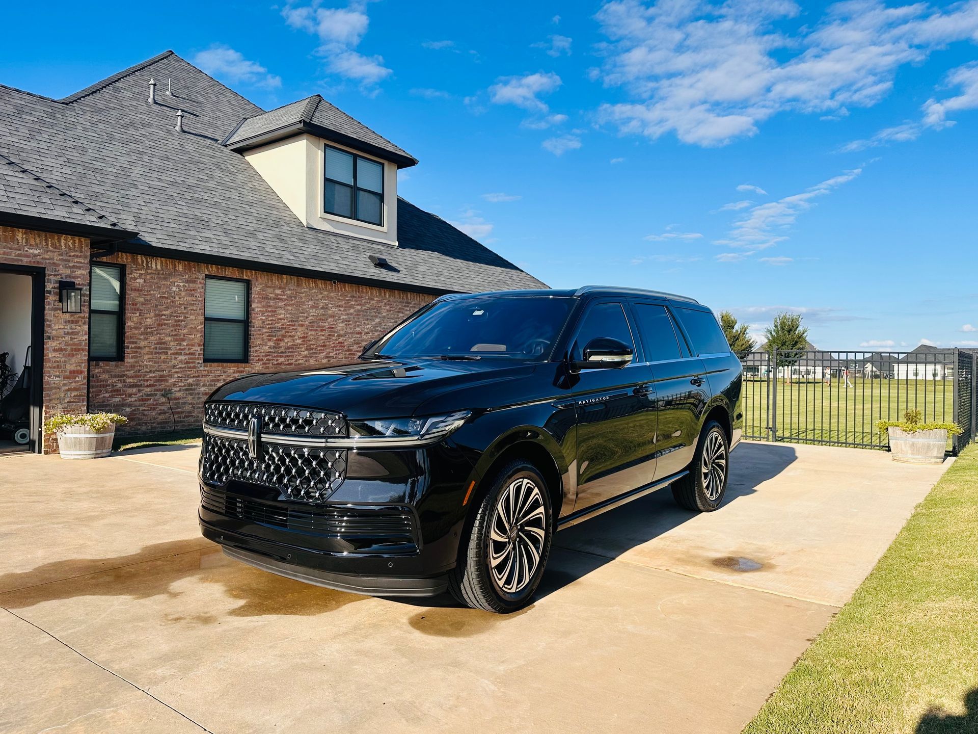Black SUV parked in a driveway beside a brick house under a blue sky