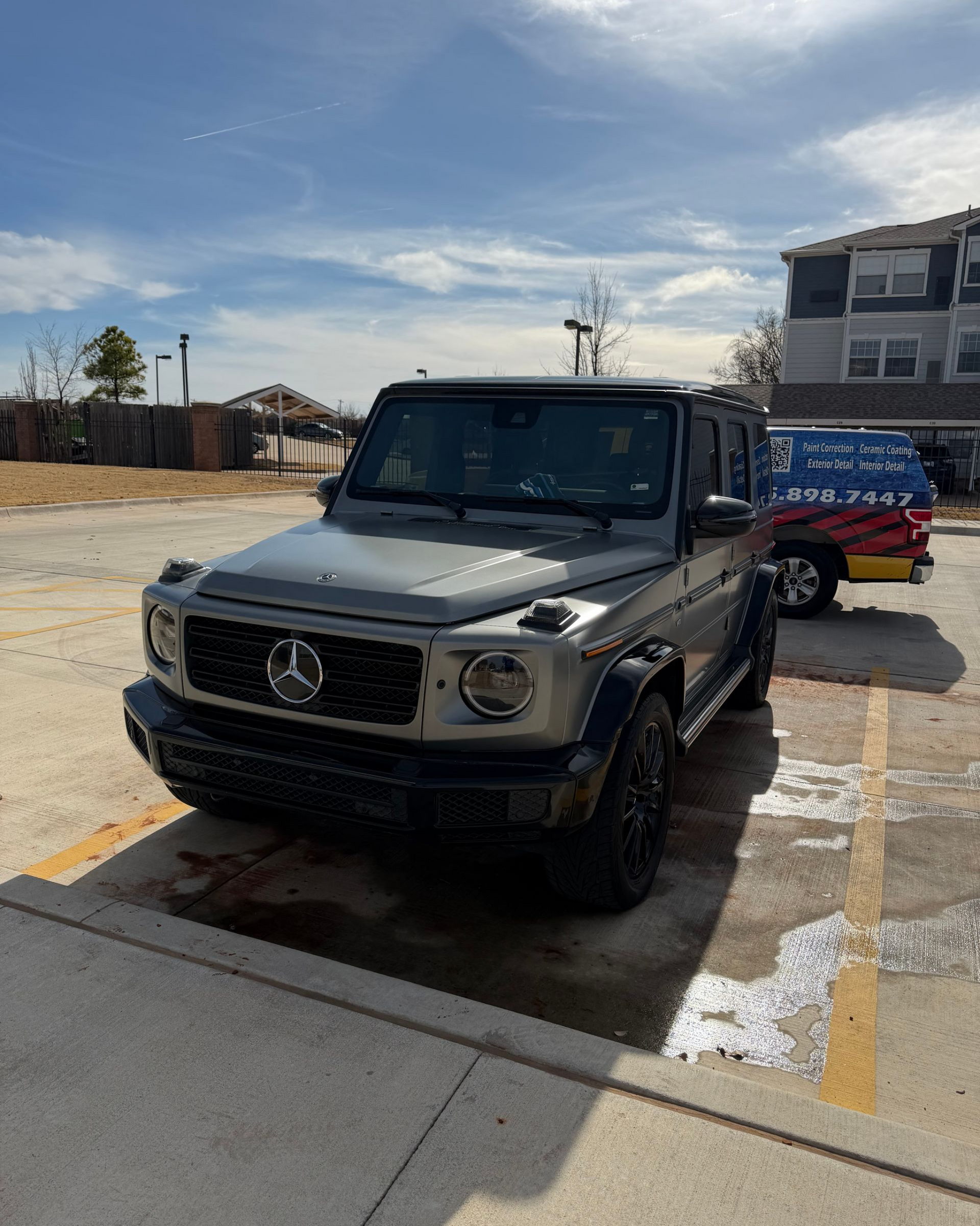 Silver Mercedes SUV parked in a sunny lot beside a building and red signboard