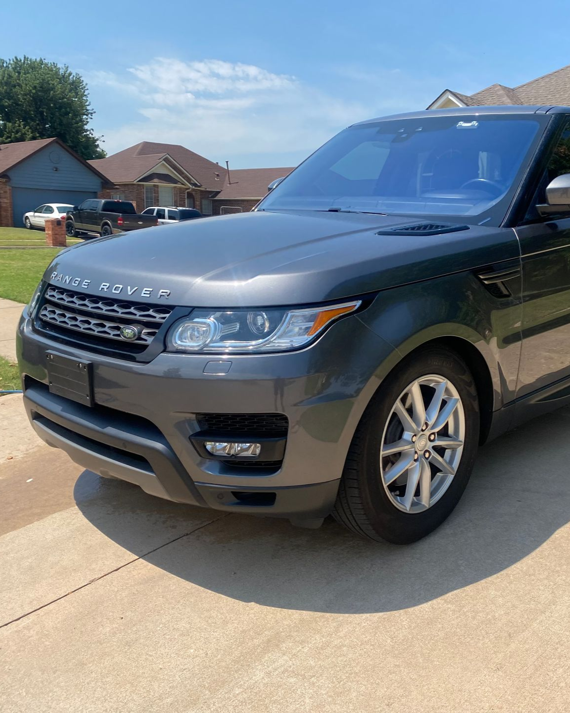 Black Range Rover parked in a sunny suburban driveway near houses