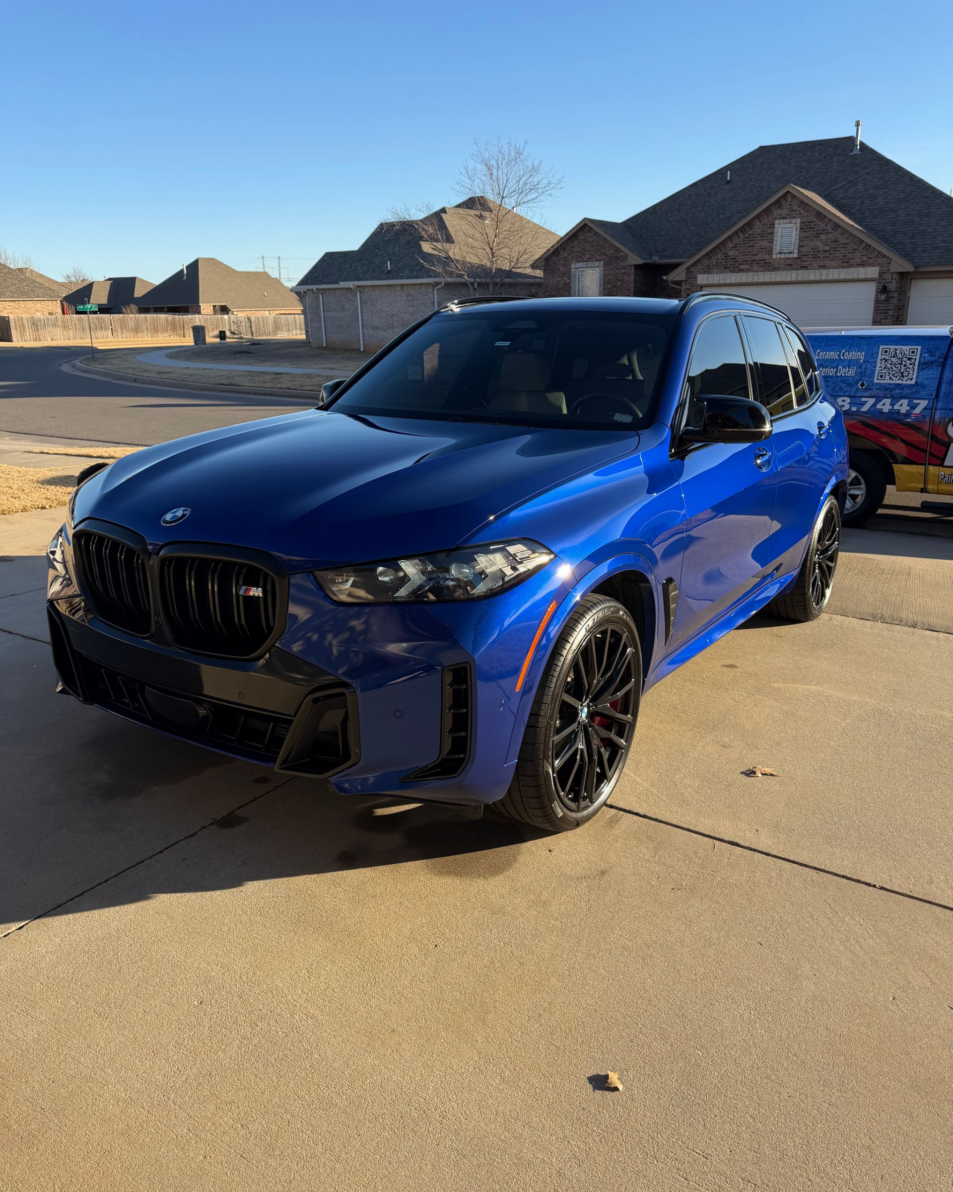 Blue BMW SUV parked in a driveway on a sunny day with houses in the background