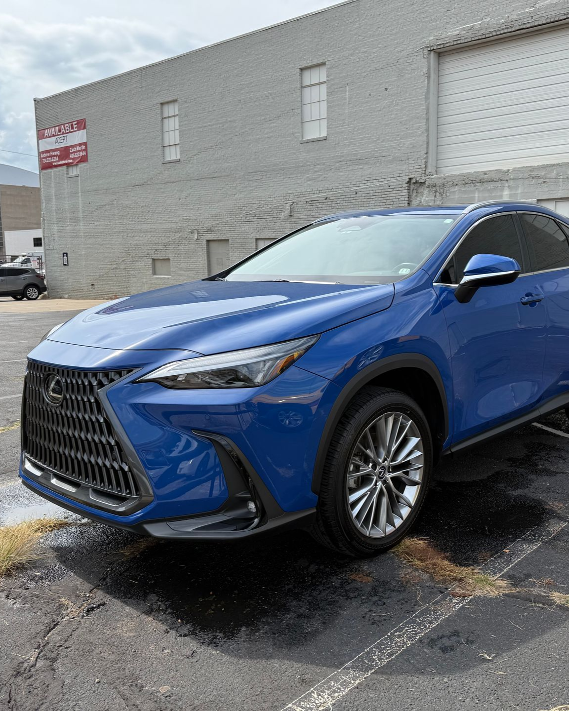 Blue Lexus SUV parked beside a gray building on a wet lot