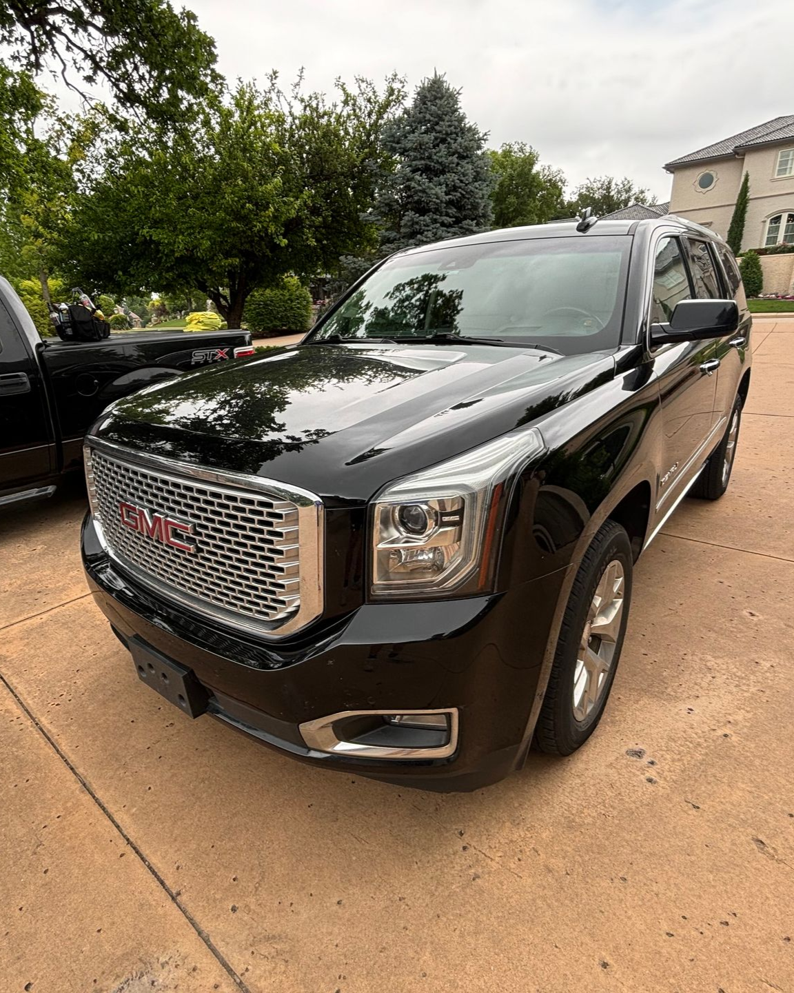 Black GMC SUV parked on a driveway, front three-quarter view, with trees and a house in the background.
