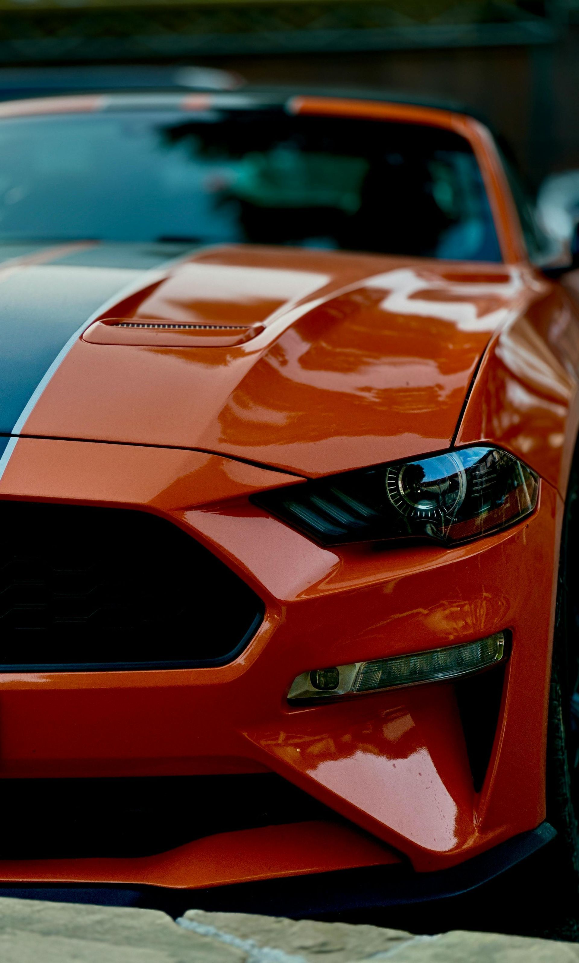 Close-up of a shiny orange sports car front end with a black grille and headlight