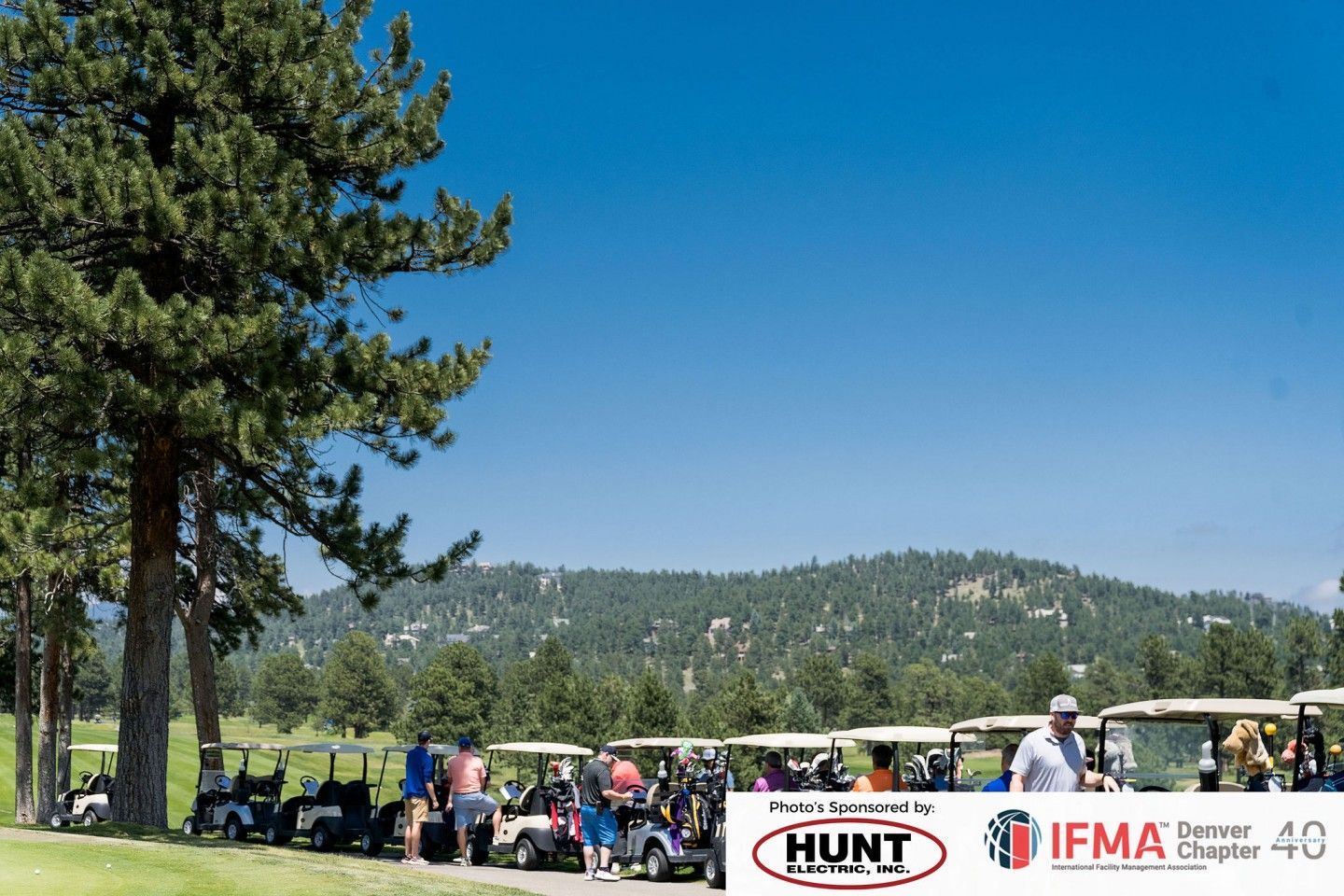 Golf carts lined up on a green, with a blue sky and mountain backdrop.