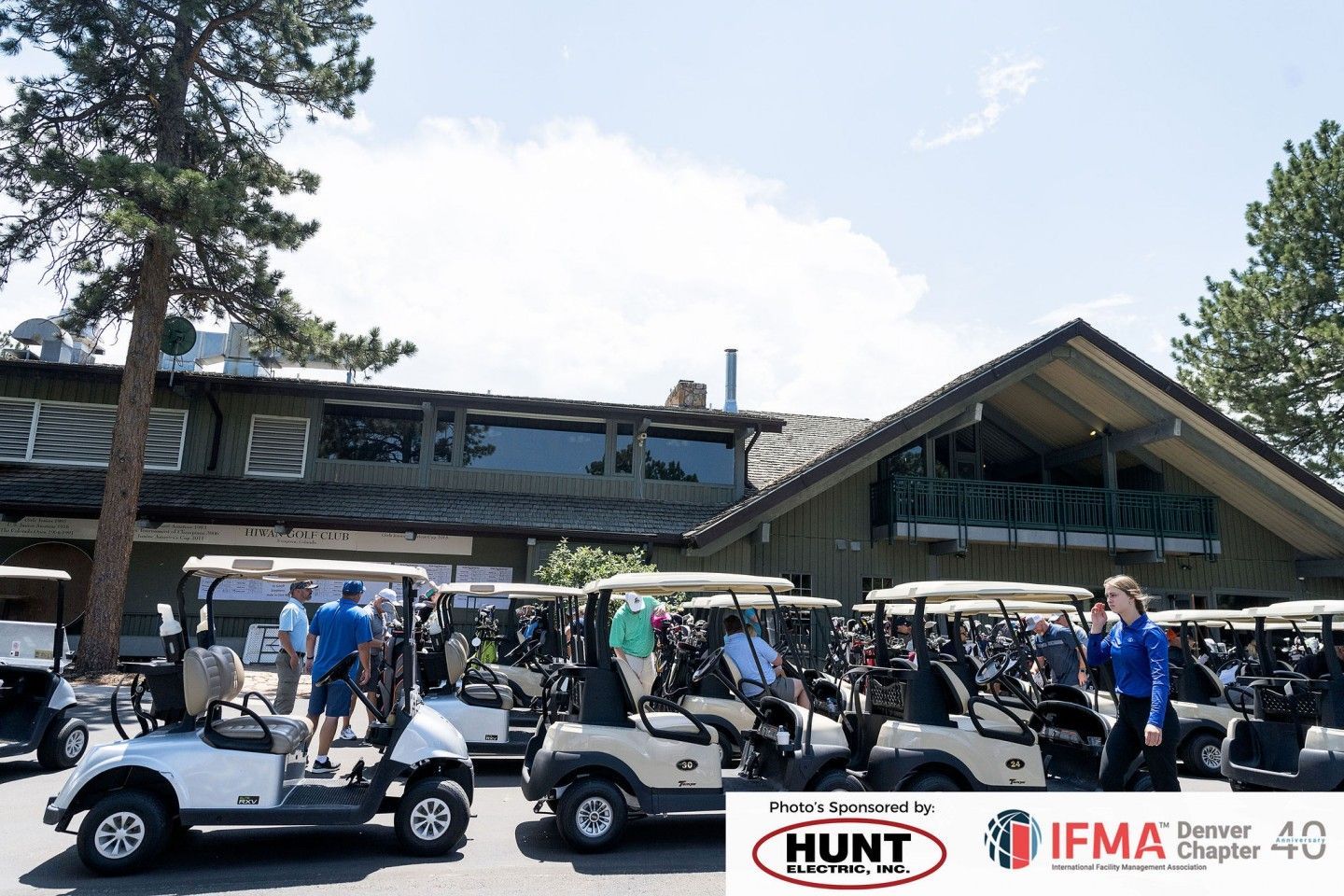 Golf carts parked outside a clubhouse. People are present. Clear, sunny day.