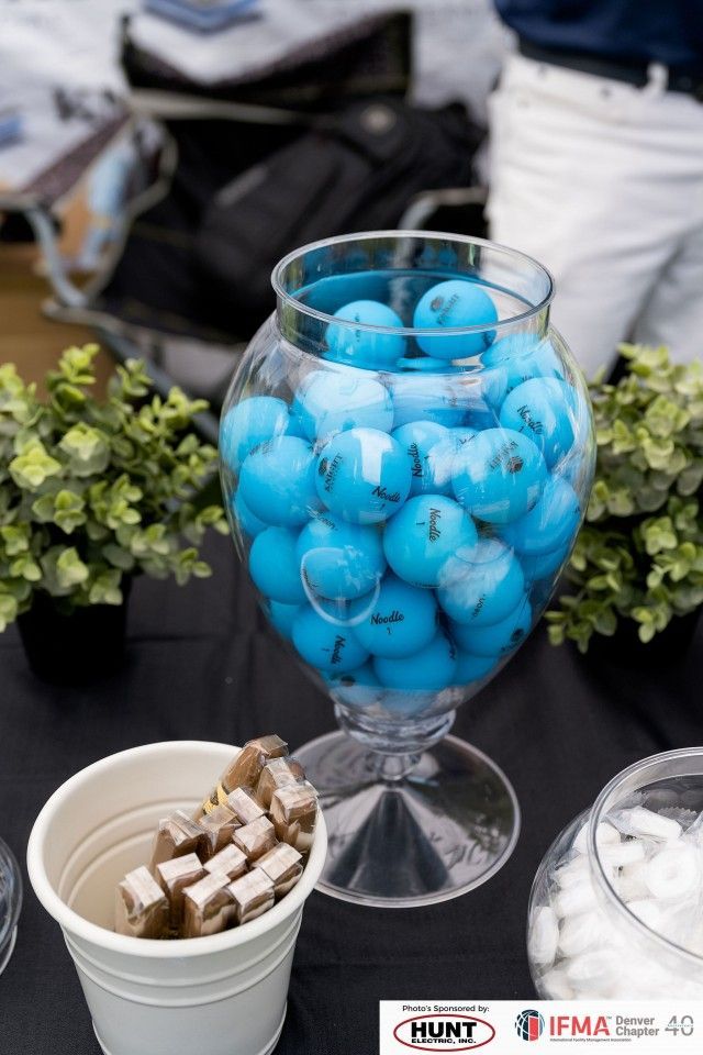 Blue golf balls in a glass jar, a container of treats, and small potted plants on a black table.