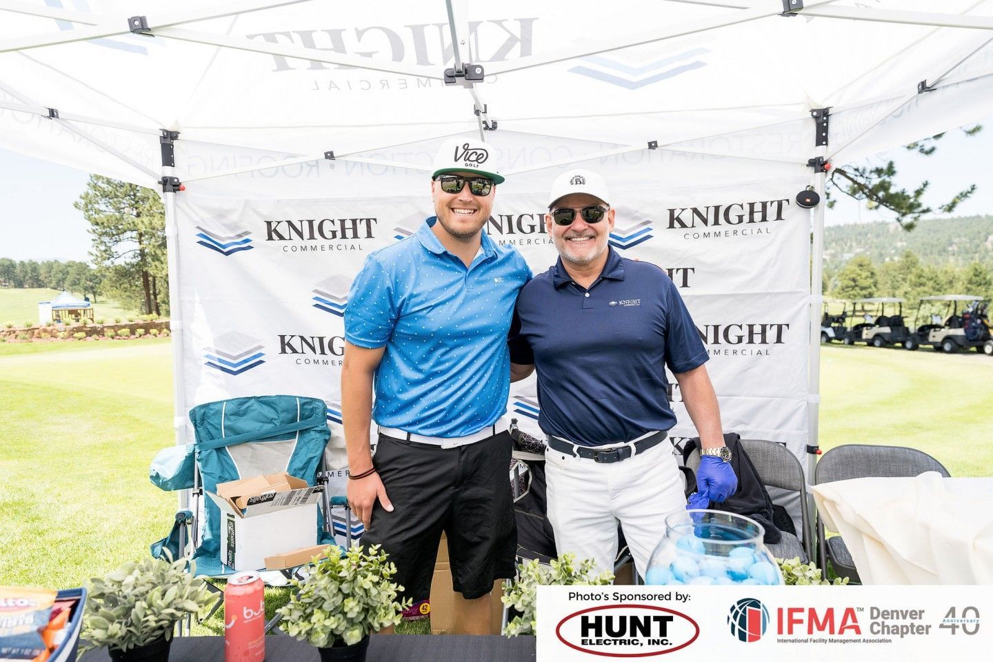 Two men smiling, posing by a Knight Companies tent at a golf event.