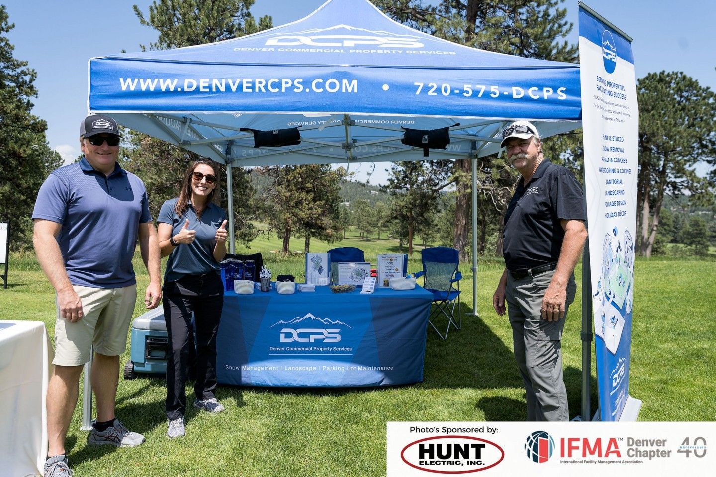 Three people stand at a Denver CPS booth at an outdoor event. A blue tent with the company's logo is set up.