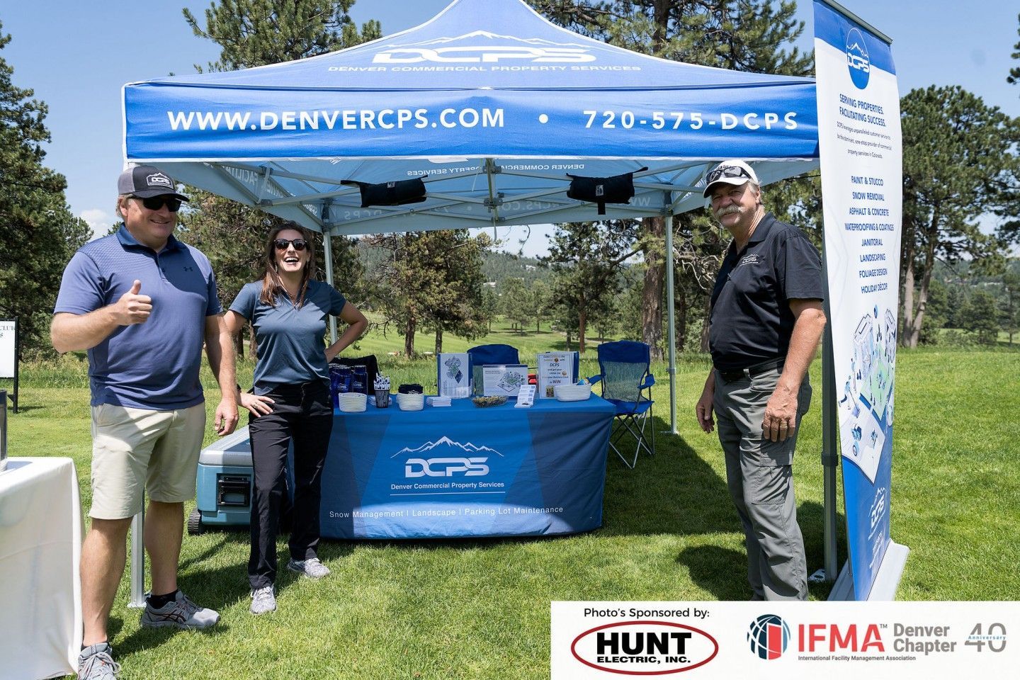 Three people stand in front of a blue booth with Denver CPS branding at an outdoor event.