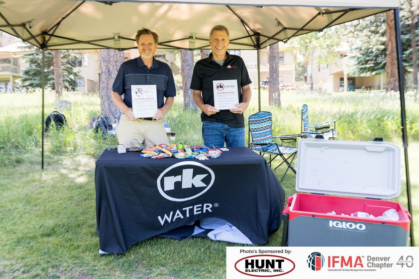 Two men at a promotional booth under a canopy with 