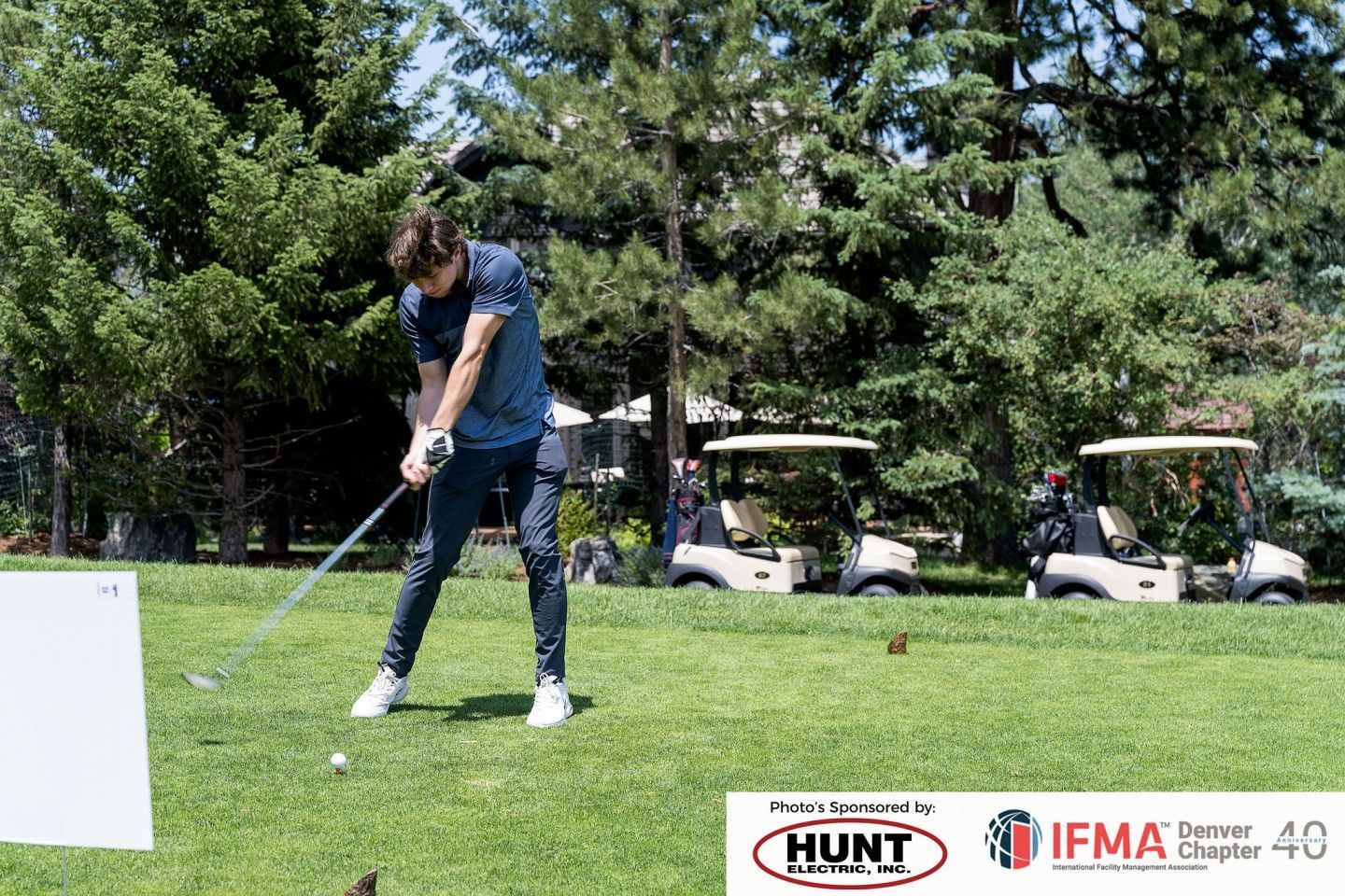 A person swinging a golf club on a green, golf carts in background.