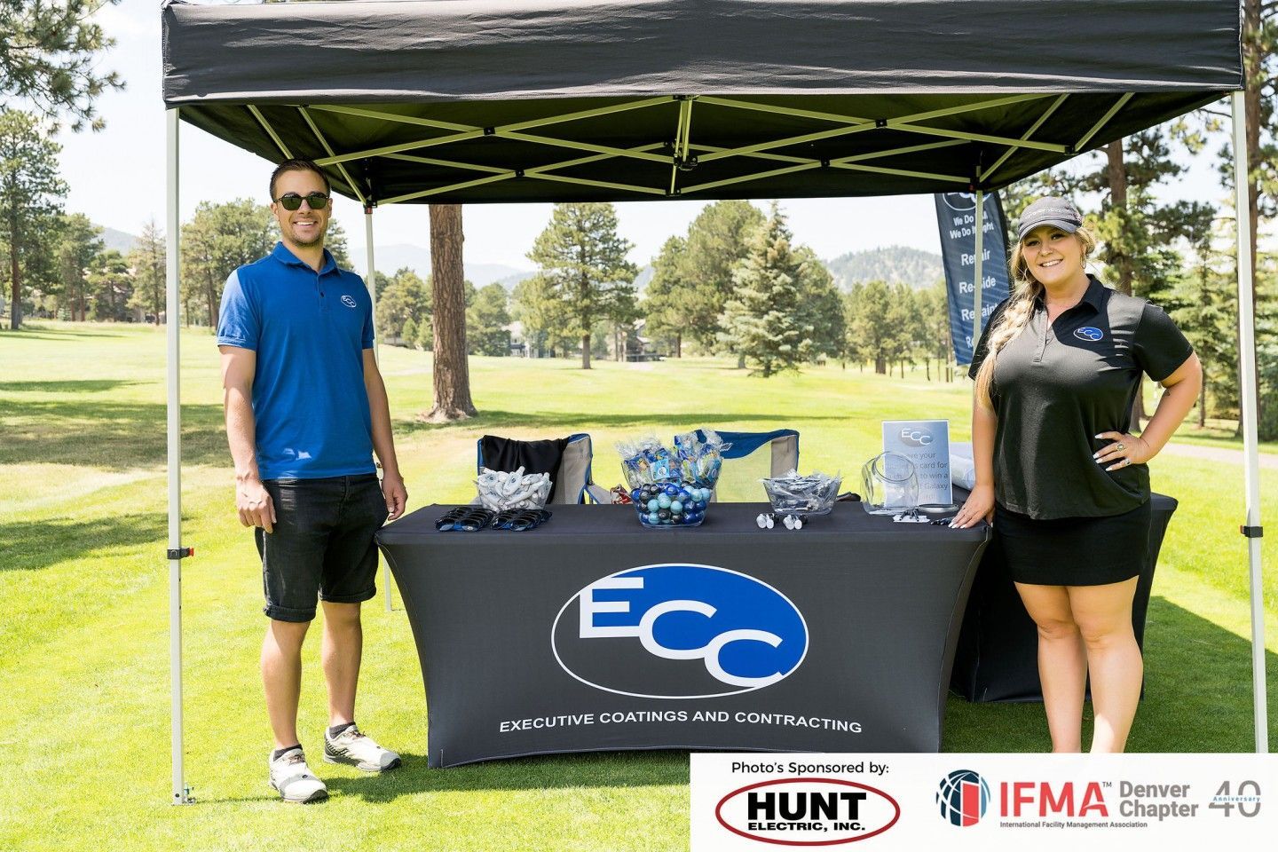 Two people at a golf event booth under a canopy, with logo 