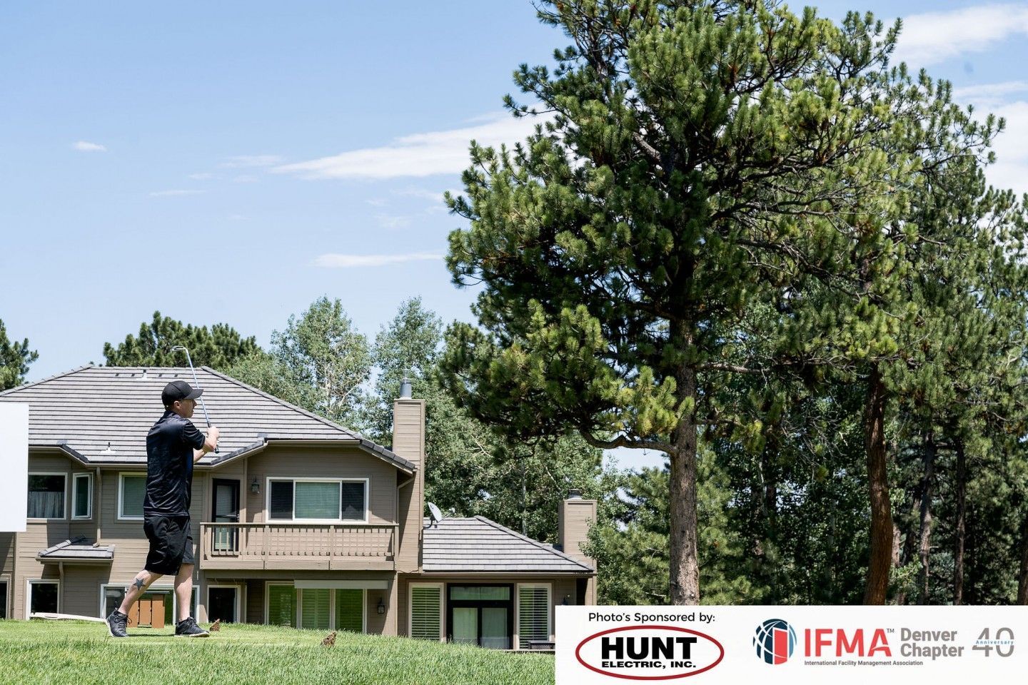 Man standing outside large house, pushing a cart on the grass. Trees and blue sky in the background.