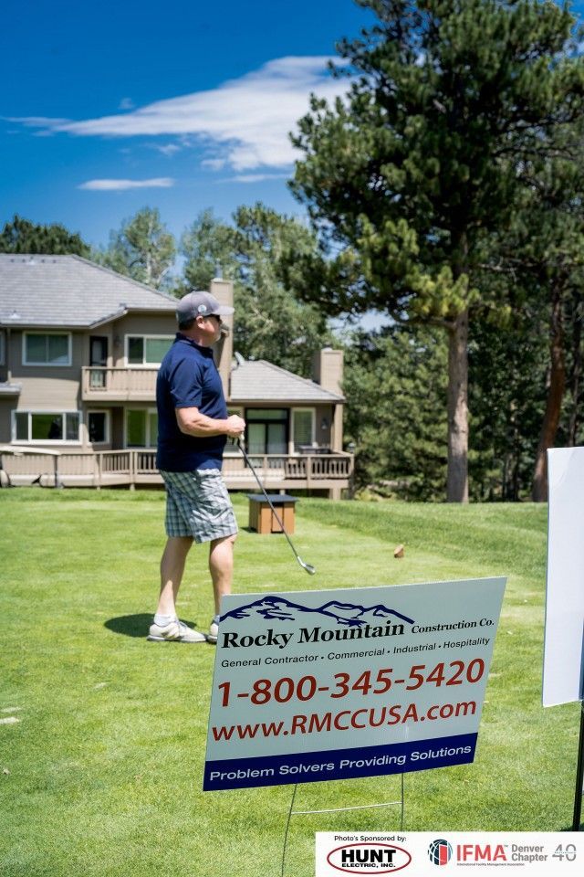Man on golf course by sign for Rocky Mountain Contractors, sunny day.