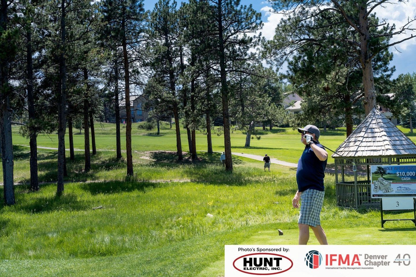 Golfer on a golf course, trees and gazebo in background. Sunny day.