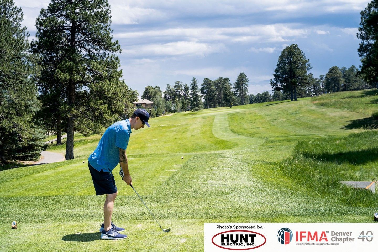 Golfer teeing off on a green fairway, trees in background, sunny day.