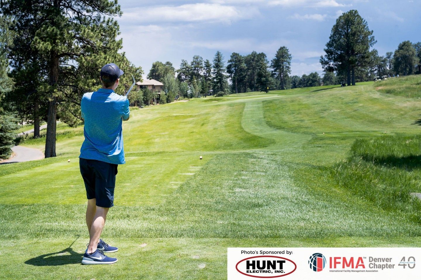 Man in blue shirt throws a disc on a grassy golf course.