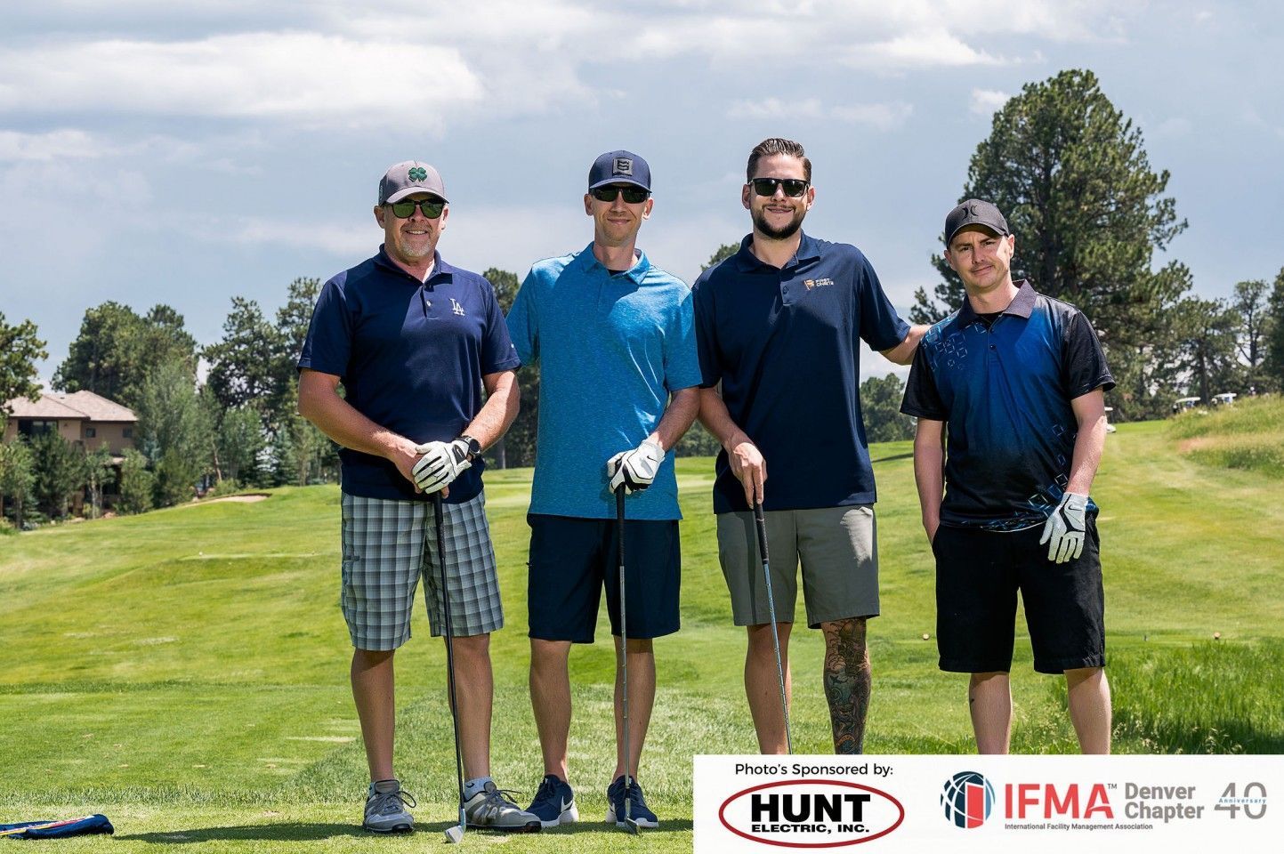 Four men on a golf course posing for a photo, sunny day.
