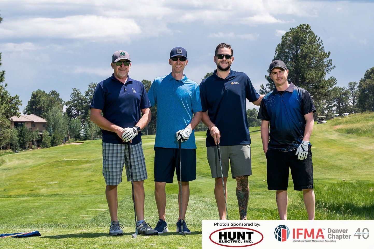 Four men standing on a golf course in summer attire, holding clubs.