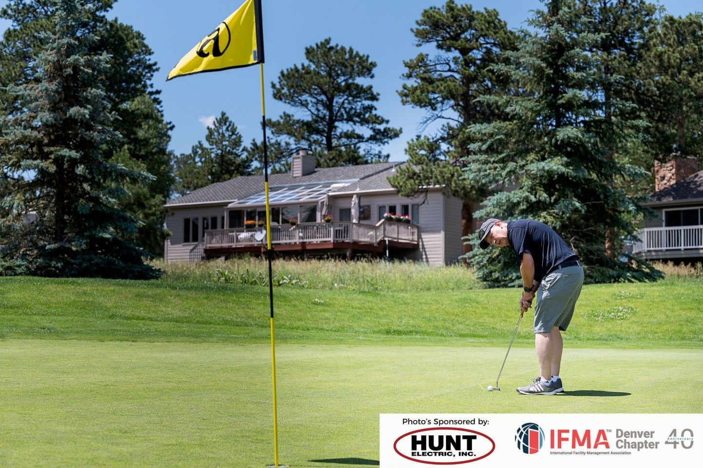 Man putting golf ball on a green, yellow flag in front of house.