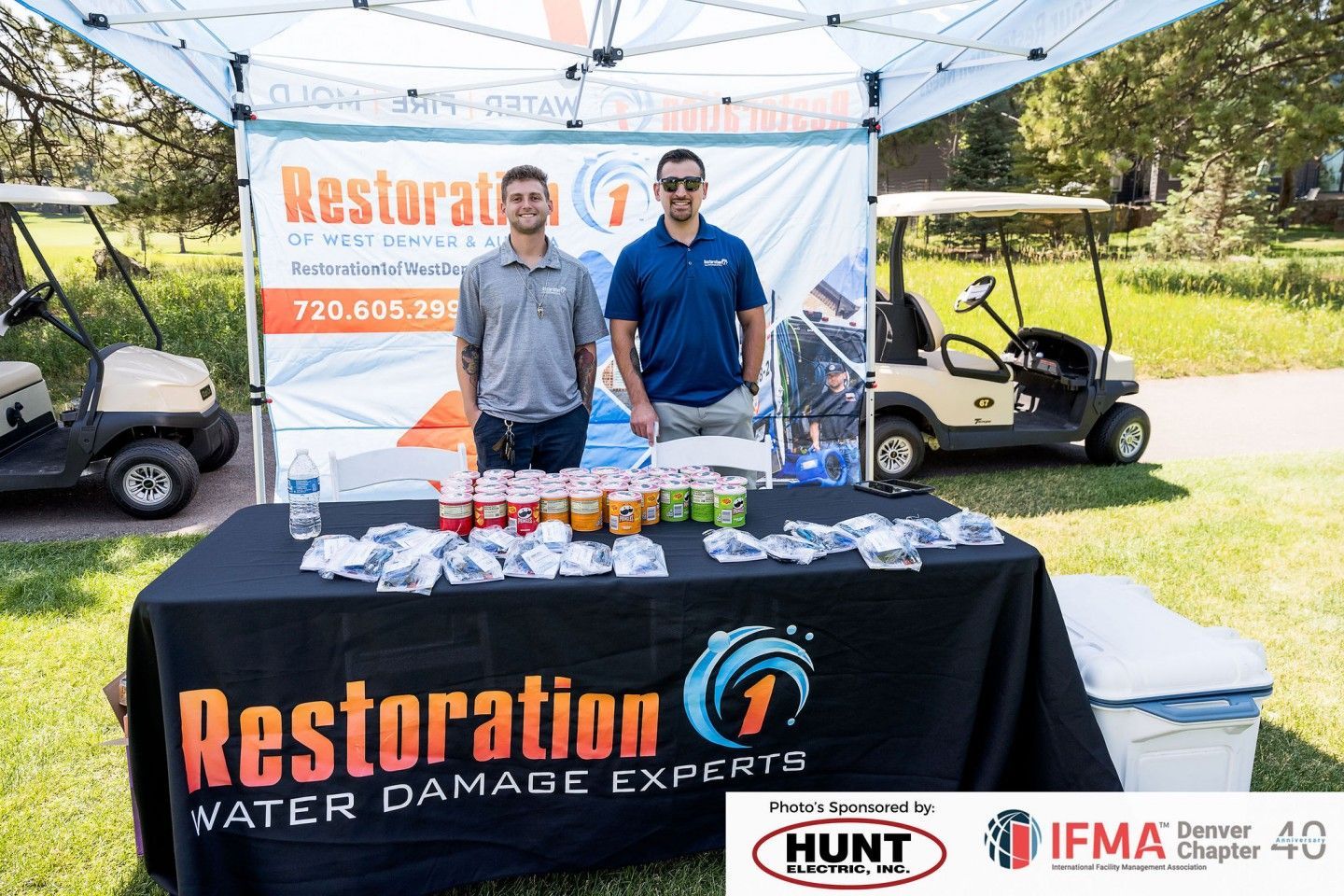 Two men at a Restoration 1 booth at an outdoor event with drinks and golf carts.