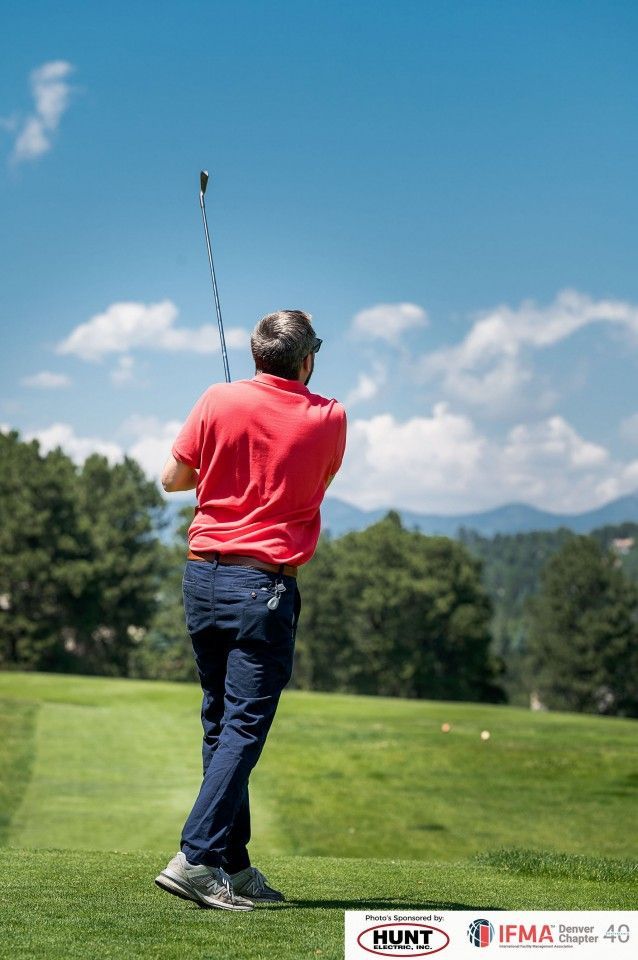 Man swinging a golf club on a green course with mountains and blue sky in the background.