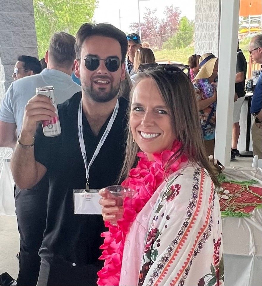 Man holding drink, woman wearing lei, both smiling at outdoor event.