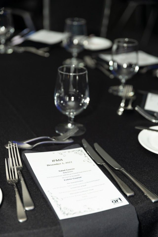 Formal table setting with black tablecloth, glassware, silverware, and menu.
